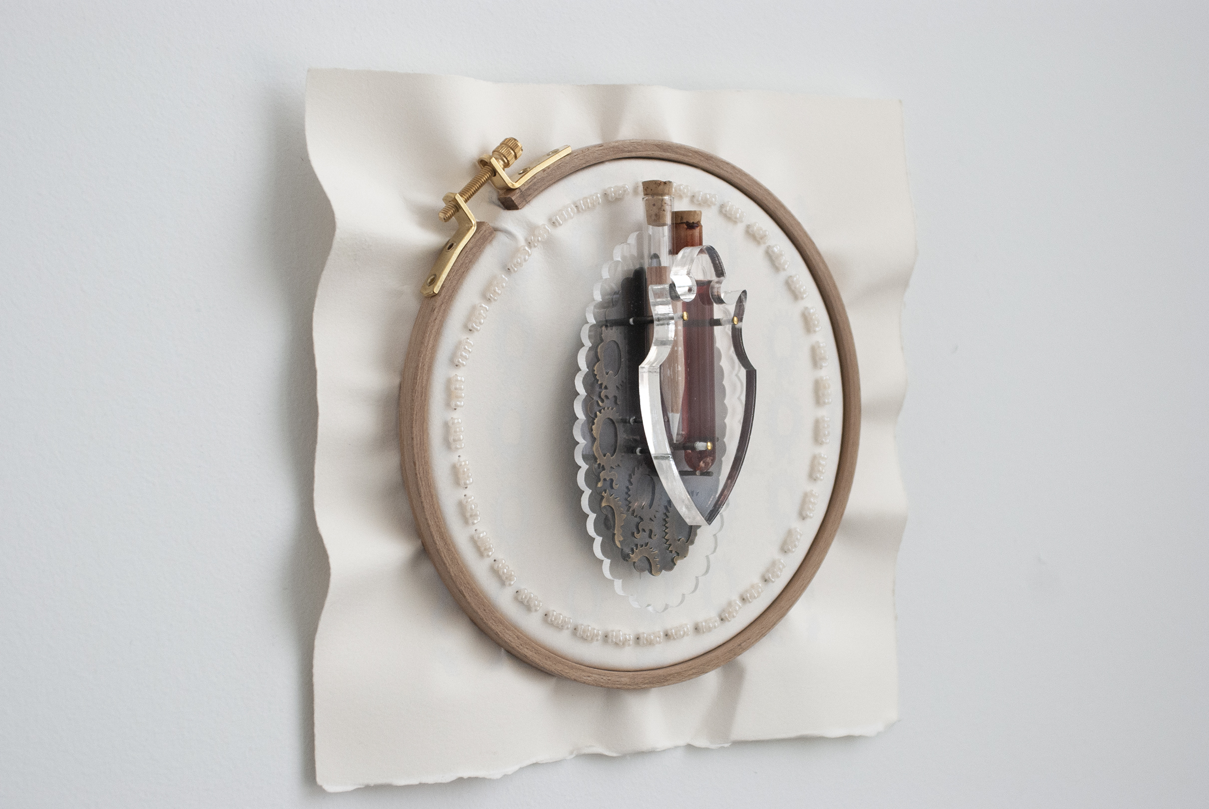 Record & Translate (Brooch) , Materials: Hand-cut and CNC-laser cut acrylic, brass with patina, swarovski crystals, prismacolor pencil, BFK Rives, wooden embroidery hoop, and beads. 2017.