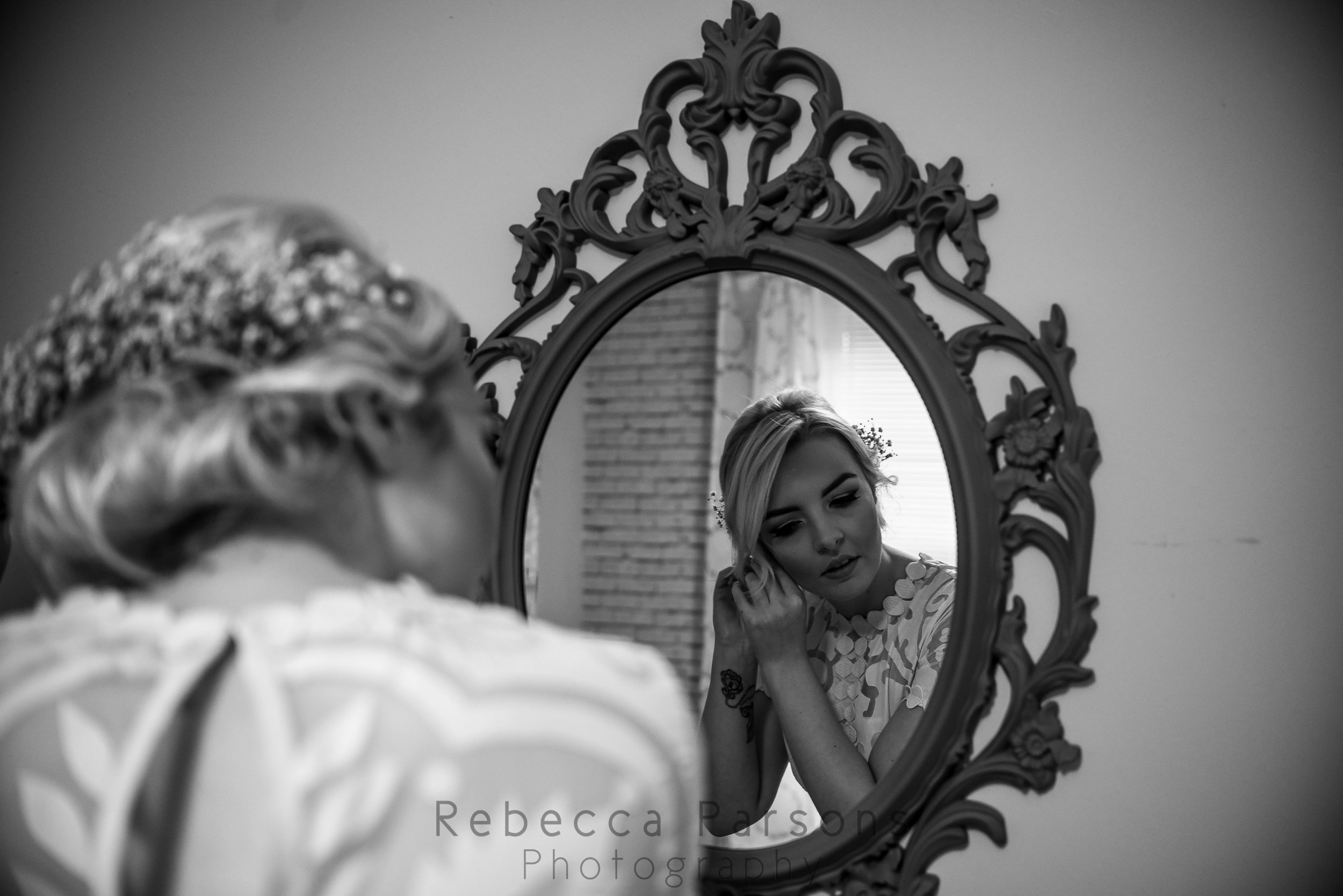 Bride putting earrings on in front of mirror black and white
