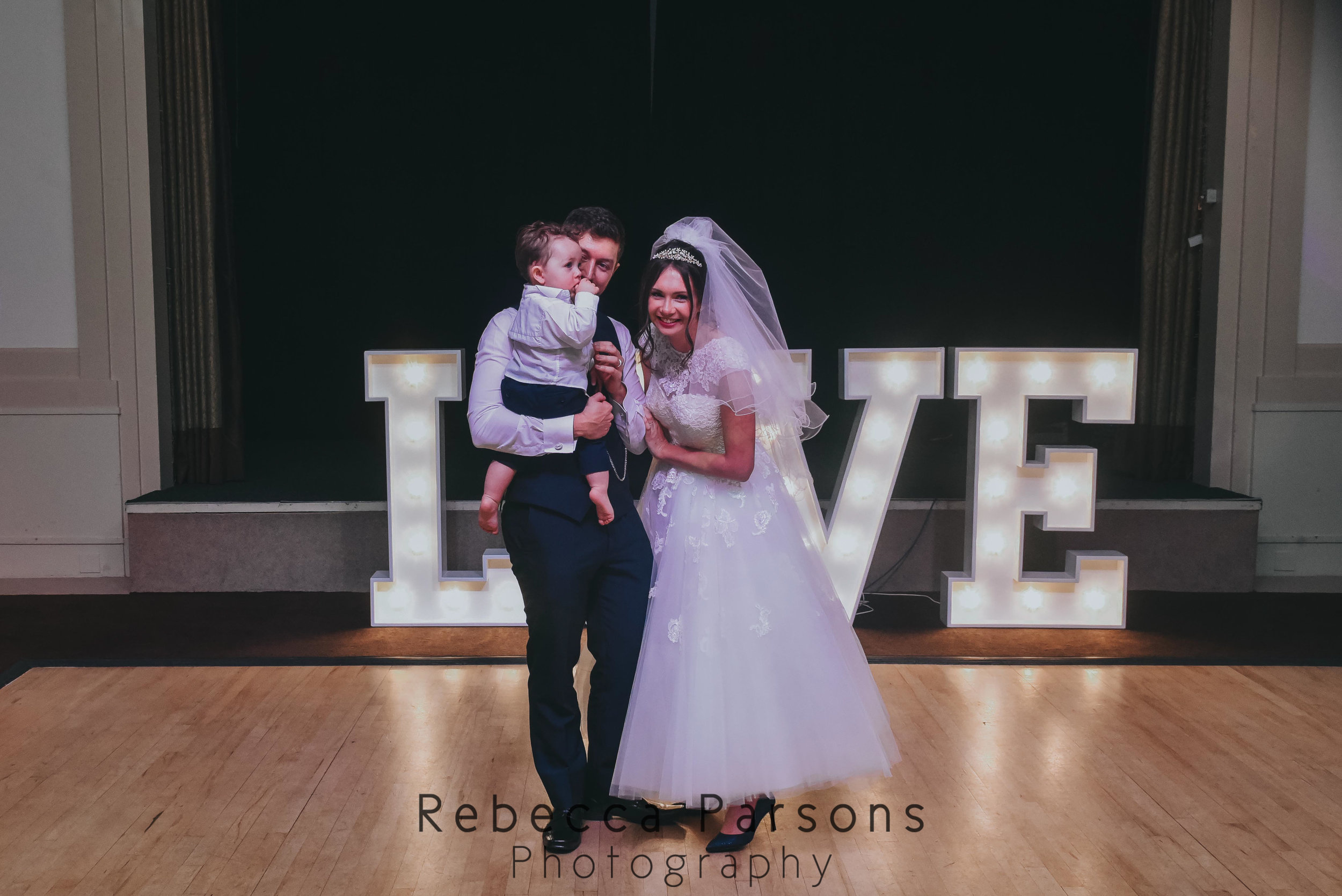 bride and groom on dancefloor with son in front of love letters