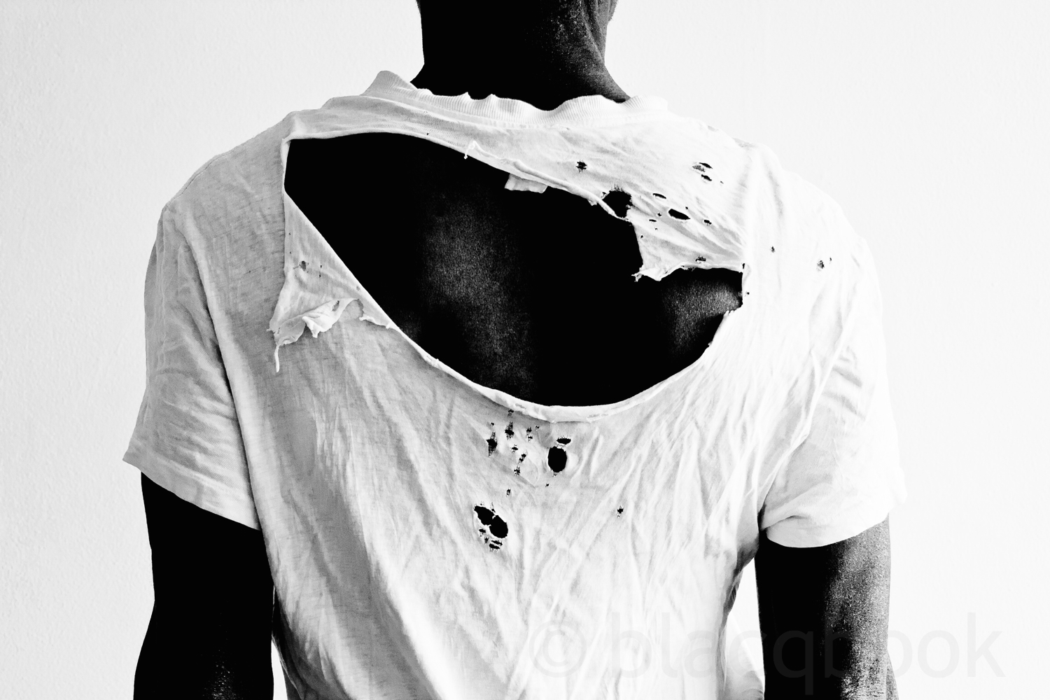 back of a man wearing a naturally distressed white t-shirt with a large hol...