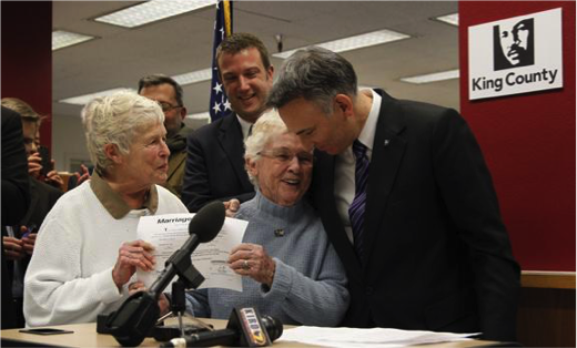Jane Abbott Lighty and Pete-e Petersen are the first to receive their marriage license, and a hug, from Executive Constantine.