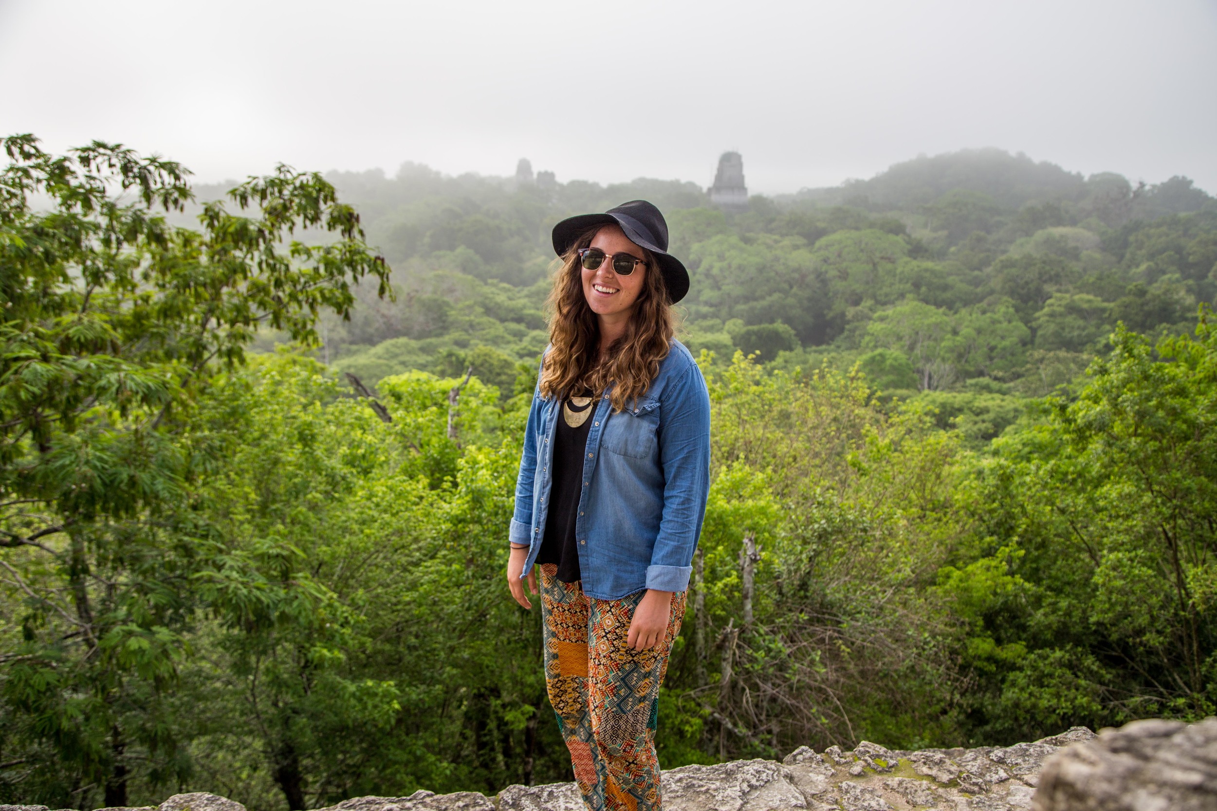 Tessa standing on the highest pyramid at sunrise. You can see the other structures coming into view over the canopy.