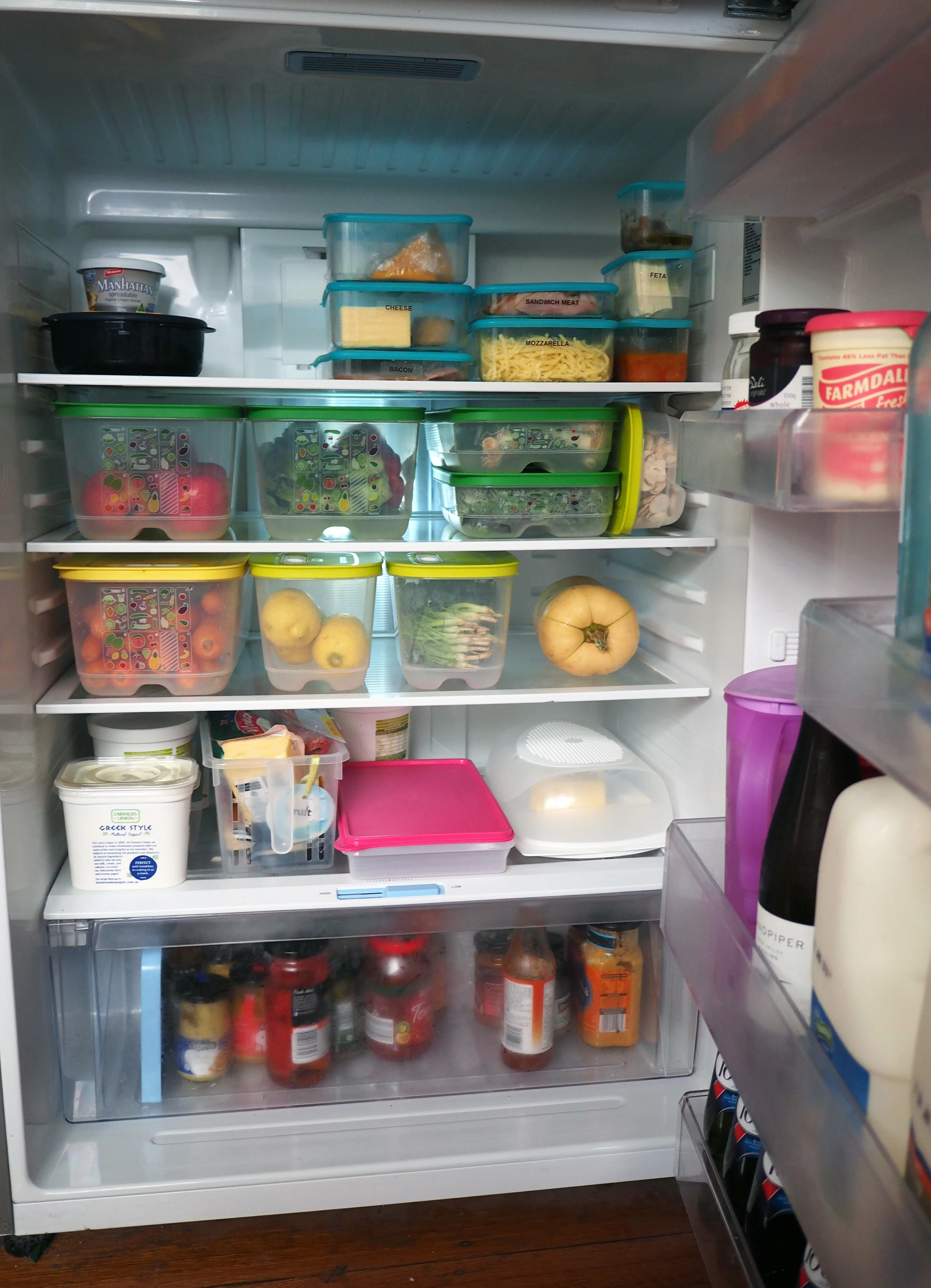 An organised fridge, using air-tight containers to seal and corral dairy items, and fruit and vegetable containers to ensure products last longer and everything is easy to find.