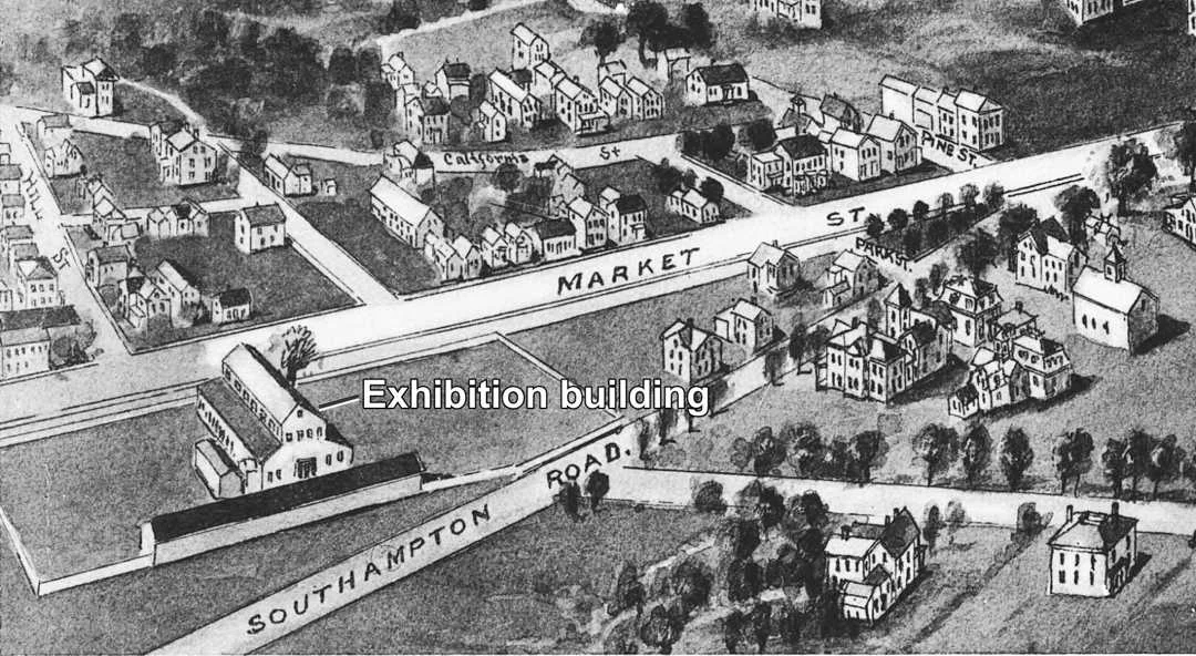 Fair grounds with exhibition building and cattle shed in a 1914 aerial view.