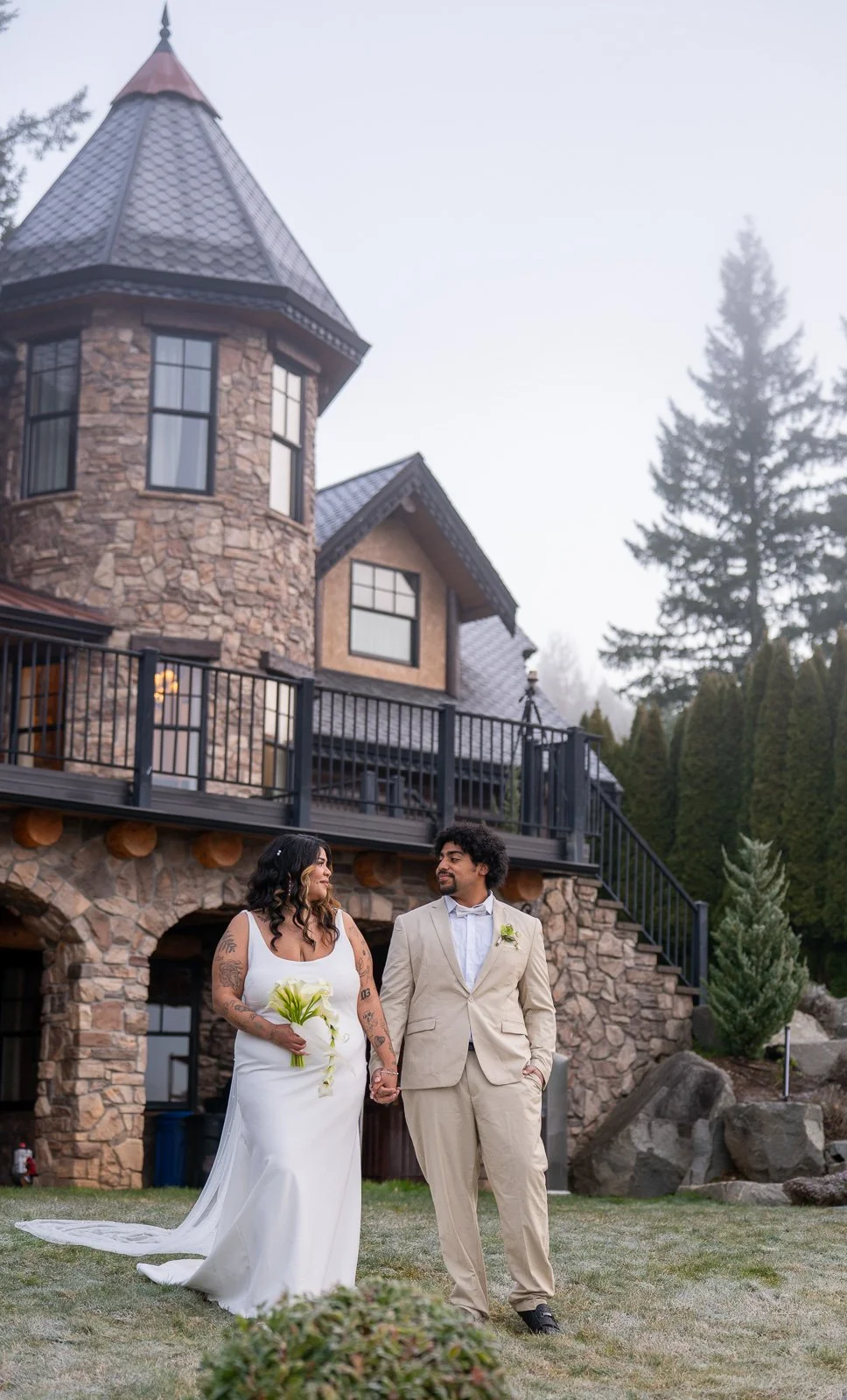Bride and groom walking together near the castle's stone turret, both laughing.