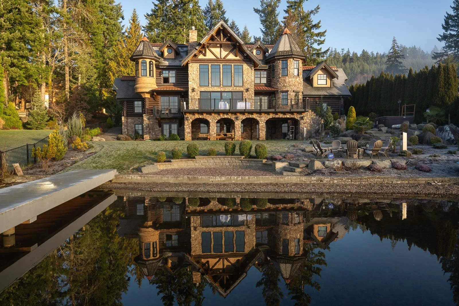 In Olympia, Washington, the Castle on Summit Lake's stone-and-log exterior with its turrets, mirrored perfectly in the still lake water at dawn.