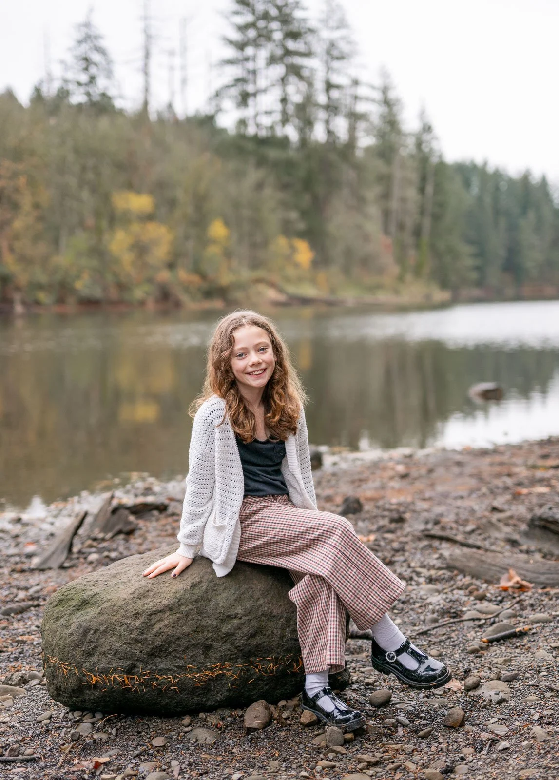 Girl sitting beside a wooded lake during an outdoor fall family photography session in Olympia, WA.