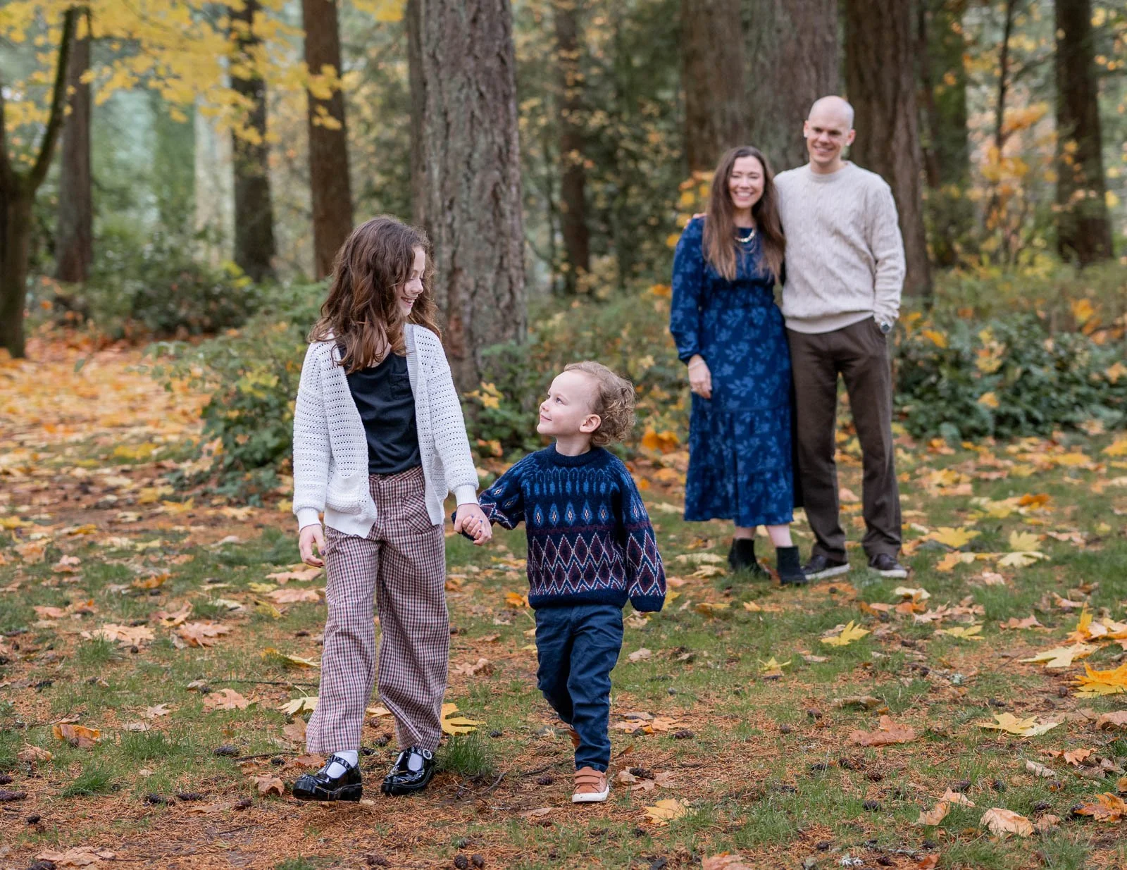 Brother and sister walking hand in hand with their parents behind them during an Olympia family photo session.