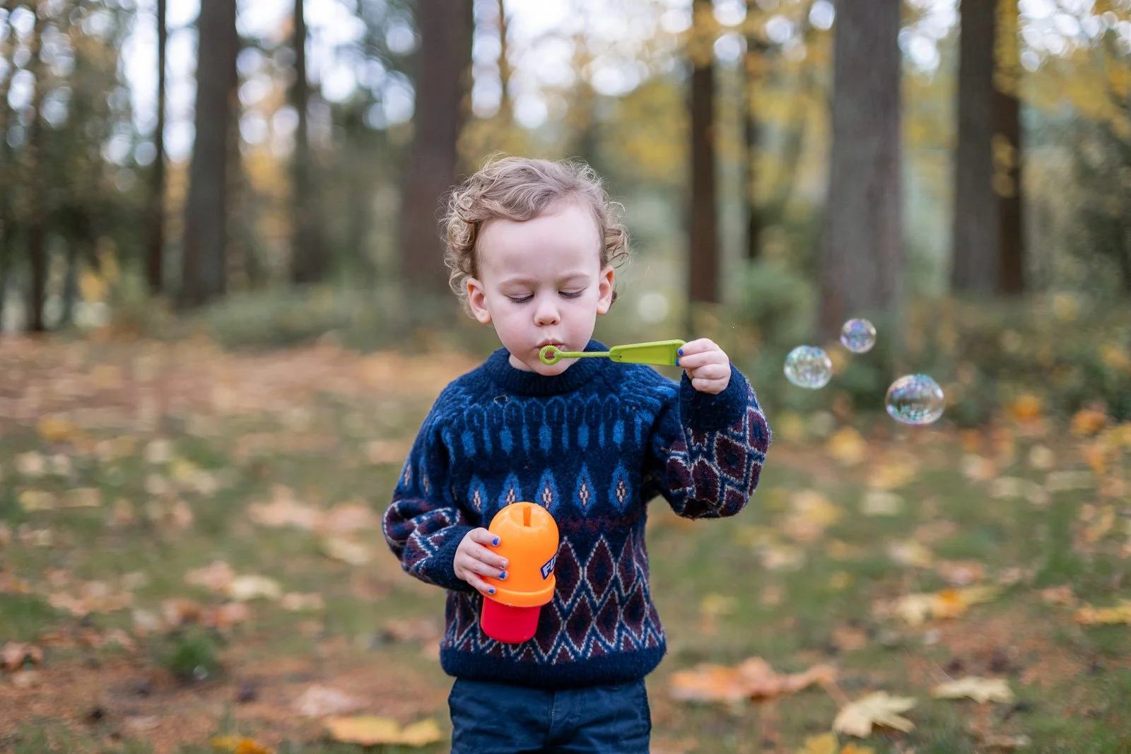 Young boy blowing bubbles among fall leaves during a candid family photography session in Olympia, Washington.