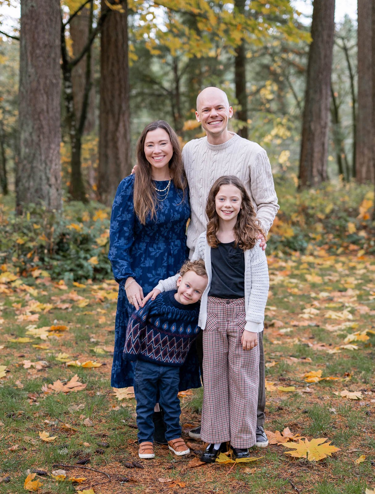 Relaxed family of four laughing together during a fall family photography session by a wooded lake in Olympia, Washington.
