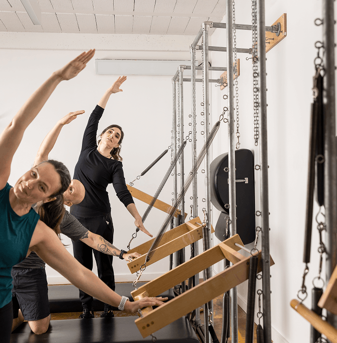 Instructor leading a Pilates class with participants on reformer machines in a fitness studio.