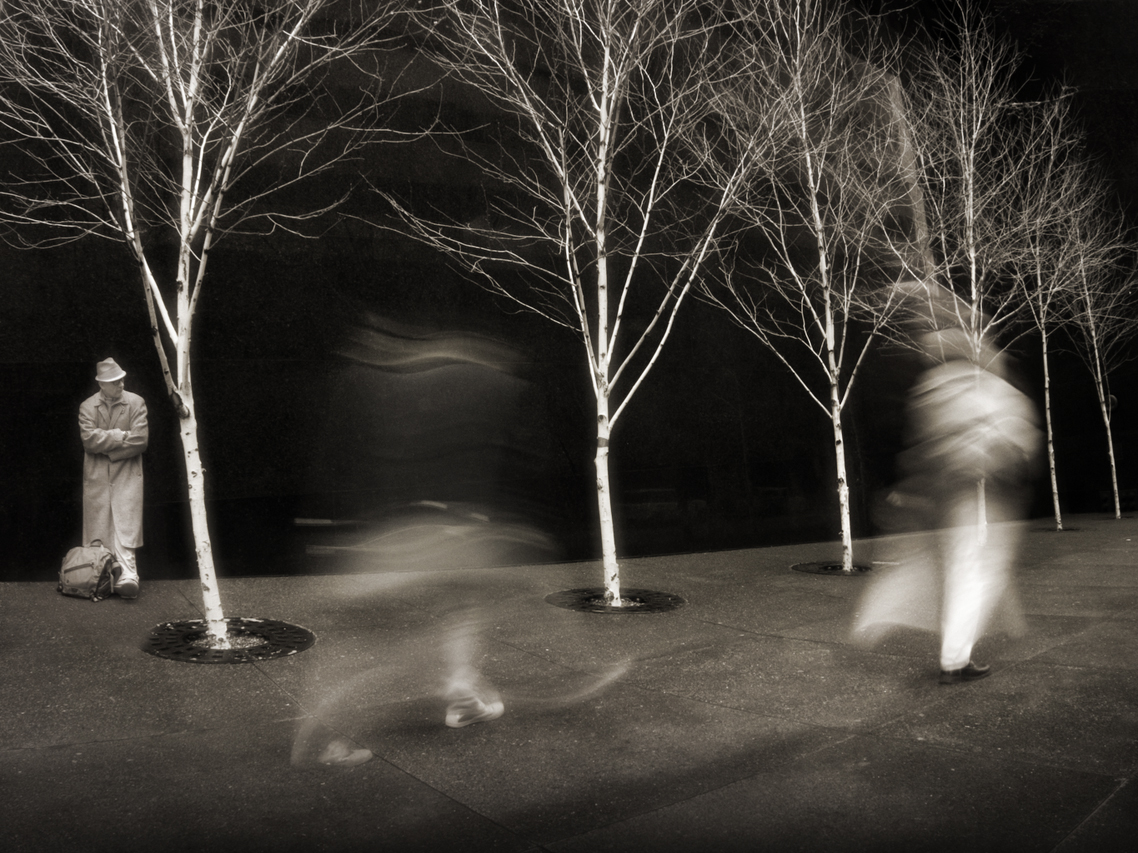 "If some longing goes unmet, don't be astonished. We call that life." -Anna Freud I was walking downtown Seattle and came across these six wonderful white-barked trees planted in front of a large, beautifully polished, black stone wall. I set up for a quick few shots and while i liked the trees, it was the people walking by that really turned out to be special. It was early evening on a week-night, the light was dropping so my exposures were on the order of 3/4 to 1 sec and as i hurriedly attempted to capture the trees and wall for my archive-of-useful-backdrops, something unexpected happened. A fellow traveler passed by in front of my lens and left behind more than just his picture - in addition, there in that soft blur, was a bit of his gait, a bit of his need-to-be-somewhere-else, a bit of his intention . So now the trees became secondary as I waited for my next wayfarer. I ended up capturing a dozen or so images. In each one was the delightful result of a slight change in temporal perspective - my every-day passers-by were transformed into dancers and thespians and sculptors and magicians. ...And that is a crowd to aspire to... Image notes: As you might expect, this image was shot in IR and that's the reason for the white clothing. It turns out that most synthetic fabrics are efficient reflectors of IR wavelengths and so show up white or very light in the image. The black shoe of my one-legged man tells me he buys leather. This guy was also wearing a rather large pack on his back - carrying, I trust, all the necessities of the day. The woman on the right was wearing a rather voluminous coat that translated wonderfully as she moved. My stillness is all well and good, but all of that motion.... 