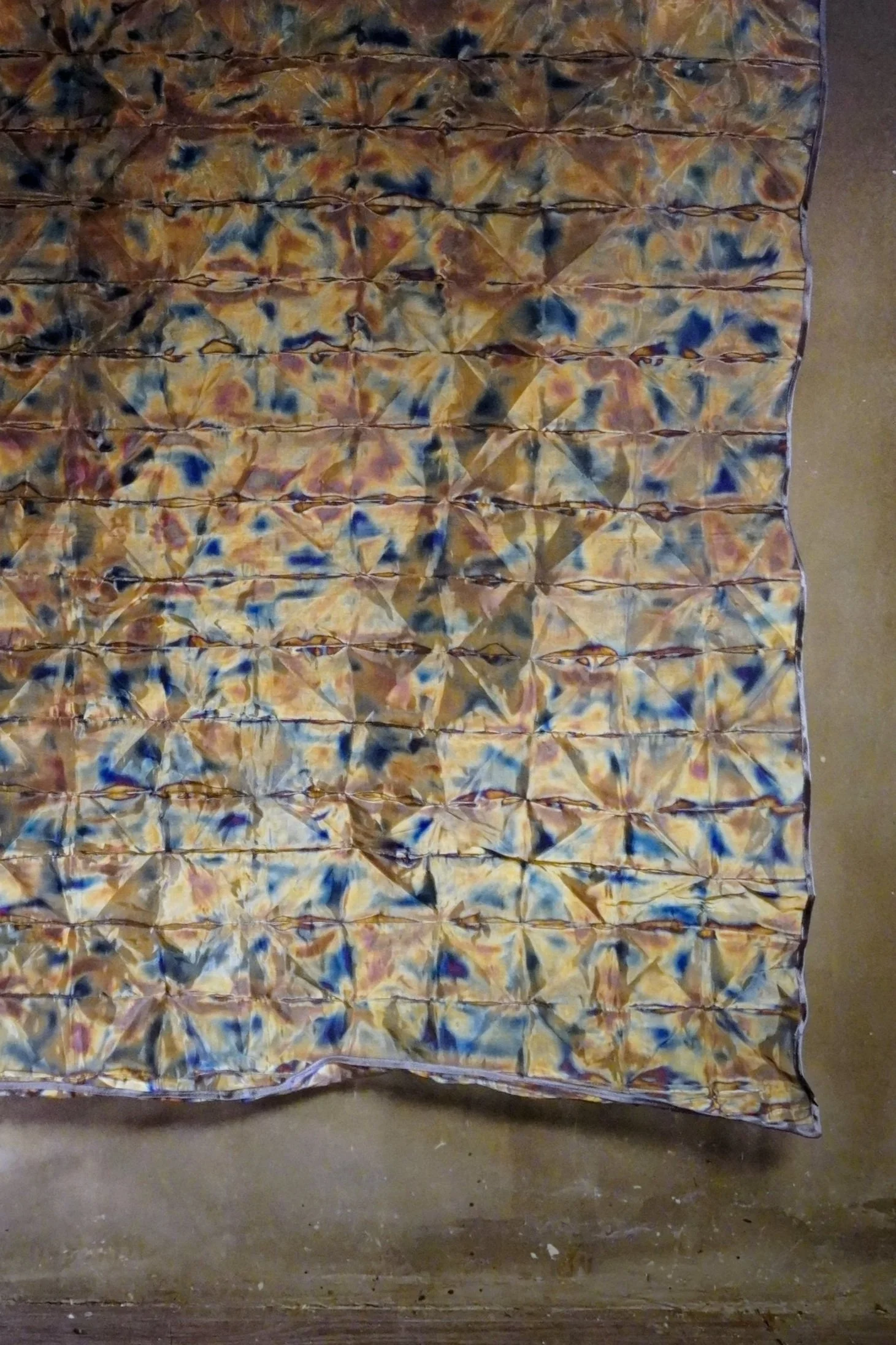 A colorful fabric with a tie-dye pattern in yellows, blues, pinks, and purples, laid out on a flat surface.