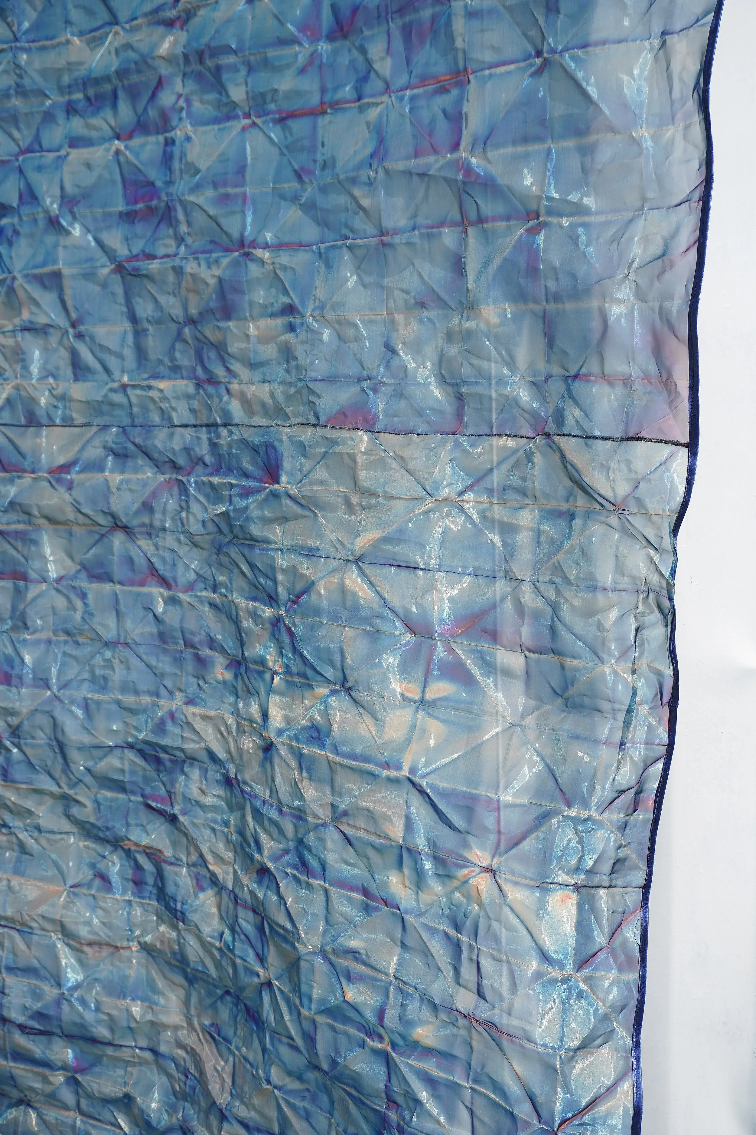 Close-up of a blue, iridescent, quilted fabric or material with a faint embroidery pattern on one side.