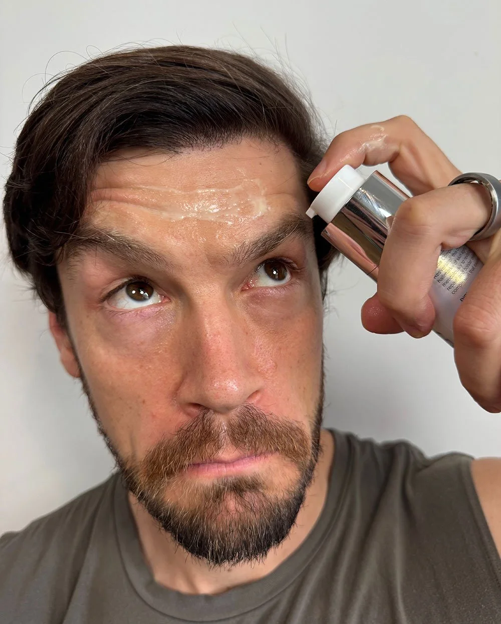 Young-Goose-Before-and-After with Nick using the skincare products on his forehead and looking upwards at the product bottle