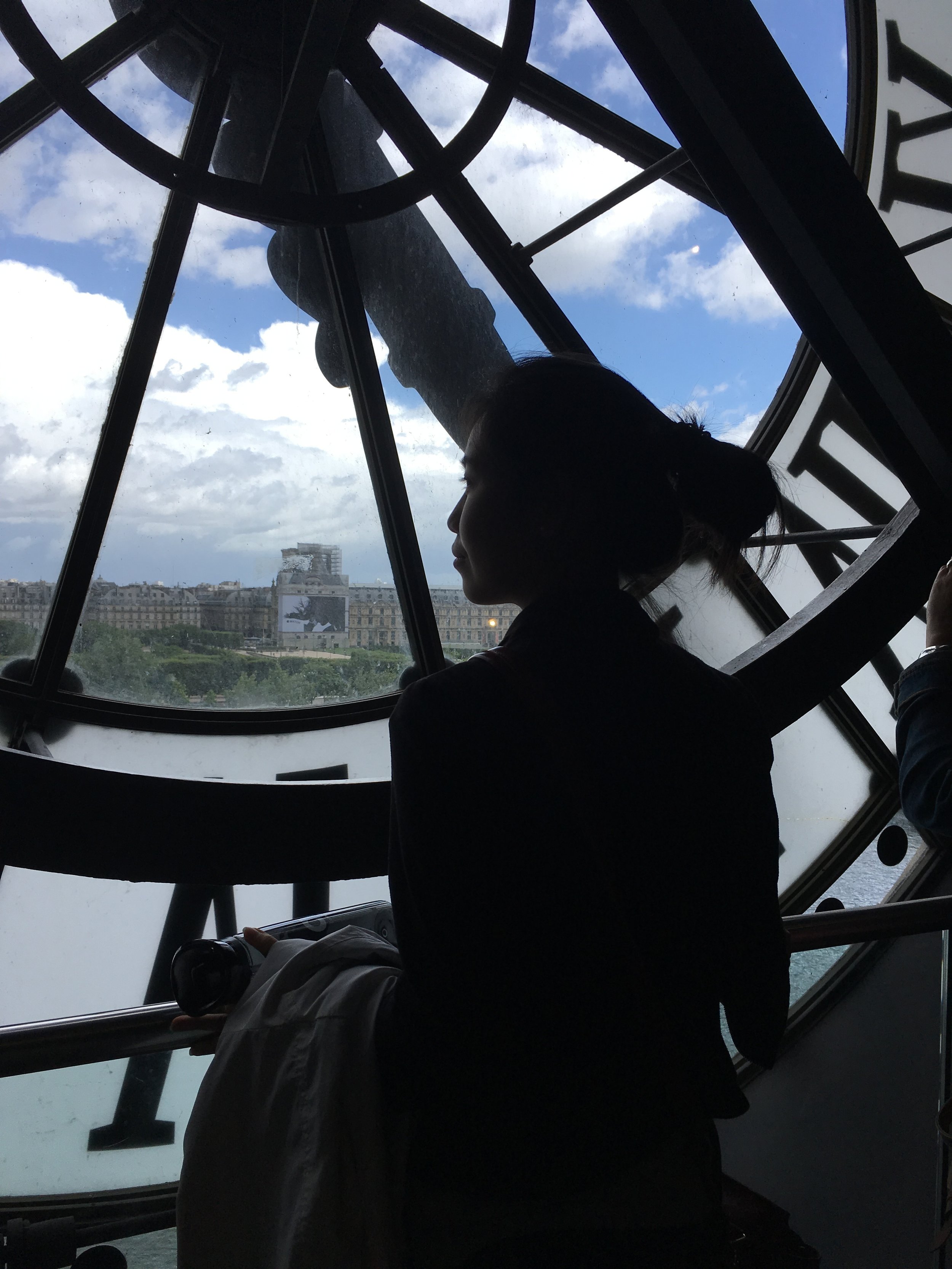 Alice in silhouette looking out onto to the Seine river towards the Louvre from the behind the famous Orsay clock. 