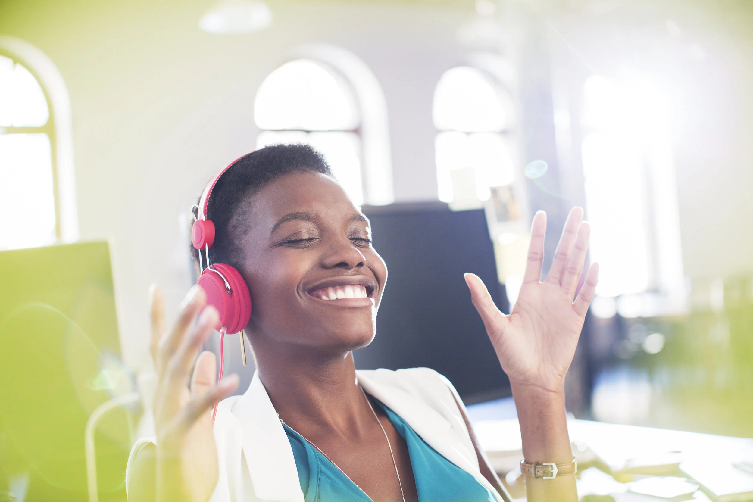 Smiling businesswoman listening to music on headphones in office eyes closed