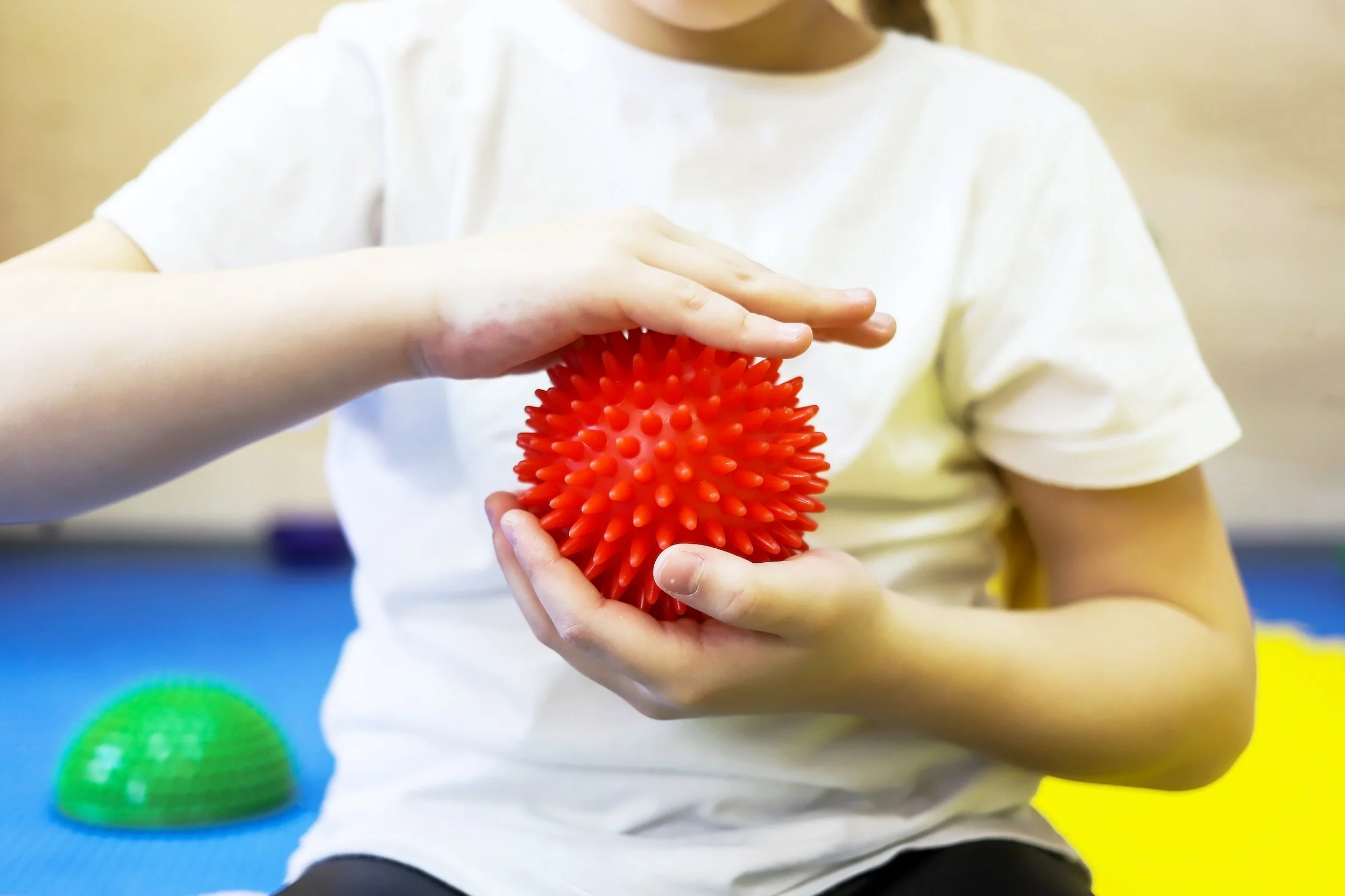 a little girl in white holds a red ball with spikes and massages