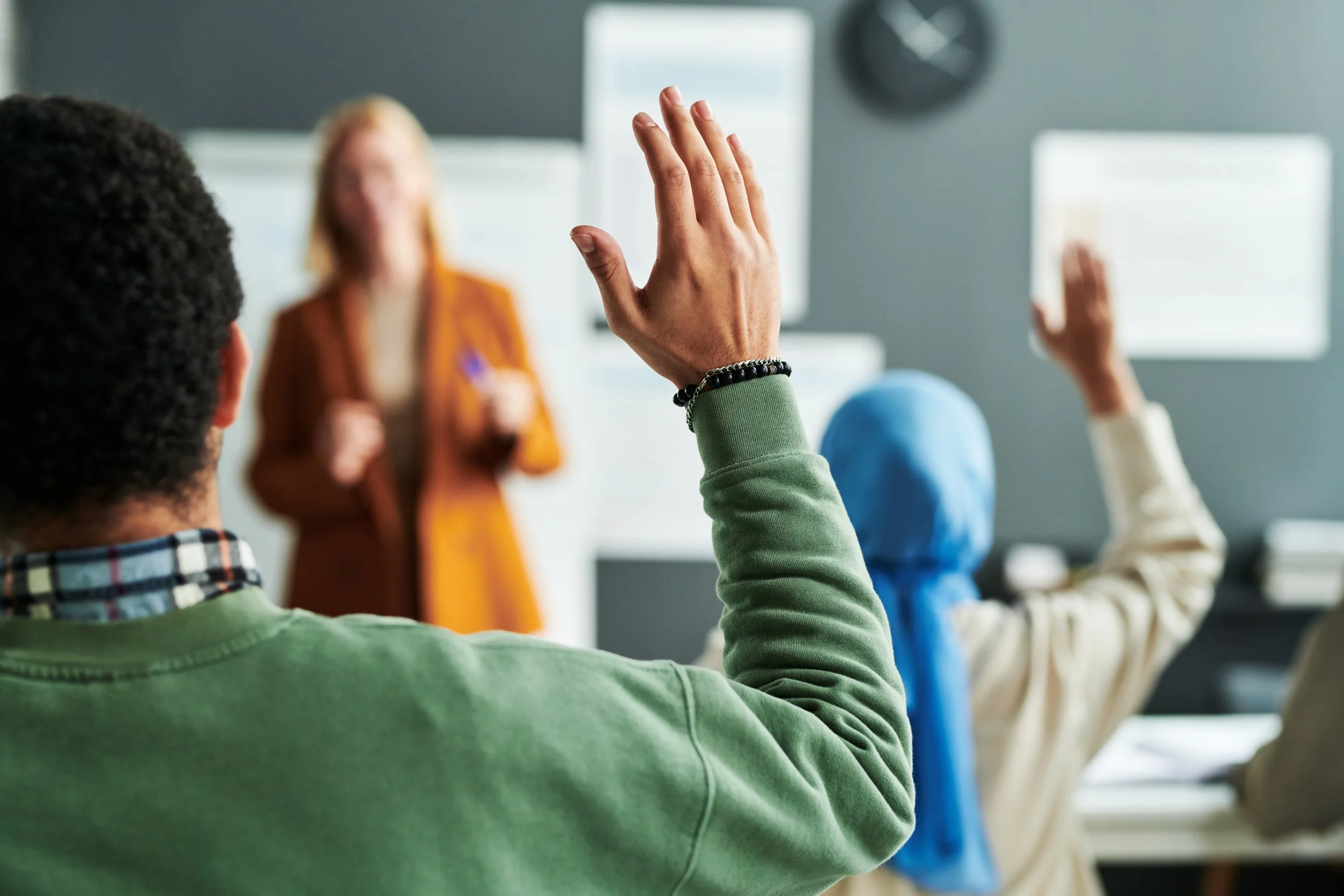 Part of back of young male student raising hand at lesson