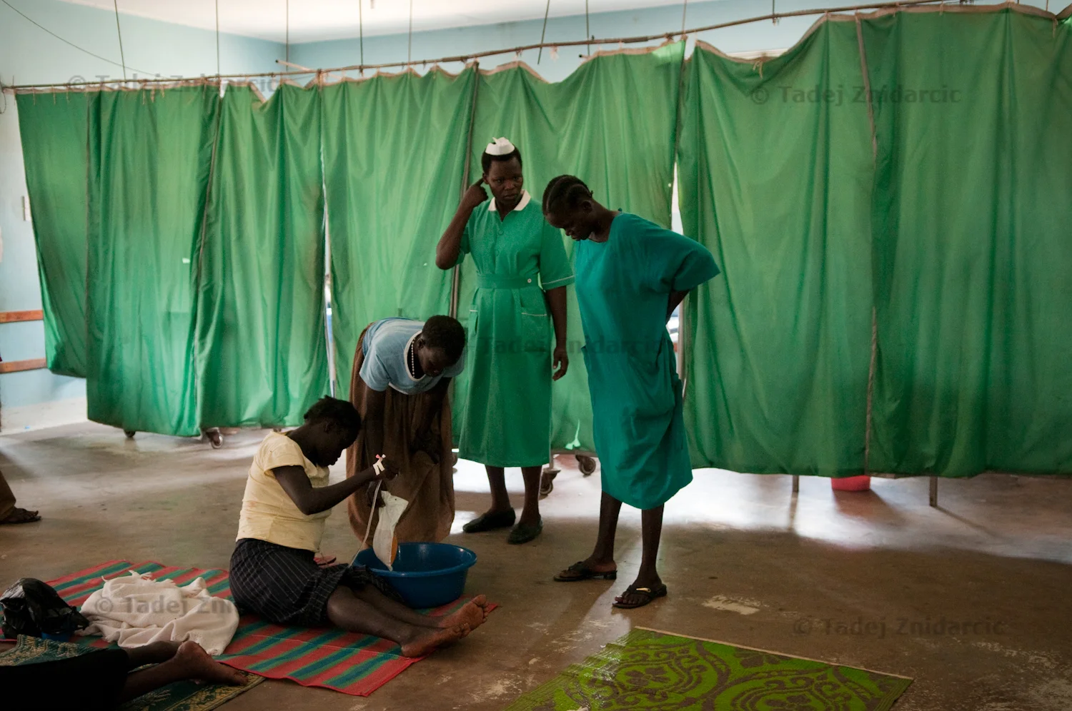 Nurses and a relative attend to a expecting mother sitting on the floor of the labor ward of Arua Hospital.