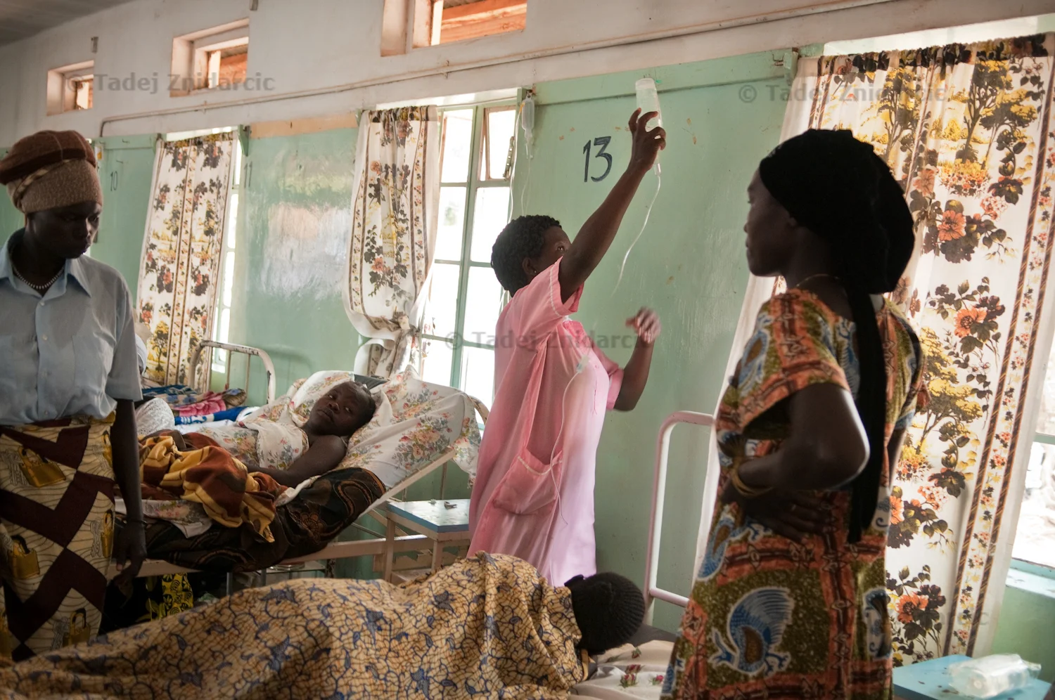 Nurse attaches IV fluid to the hook on the wall in the postnatal ward of maternity ward of Arua Hospital.