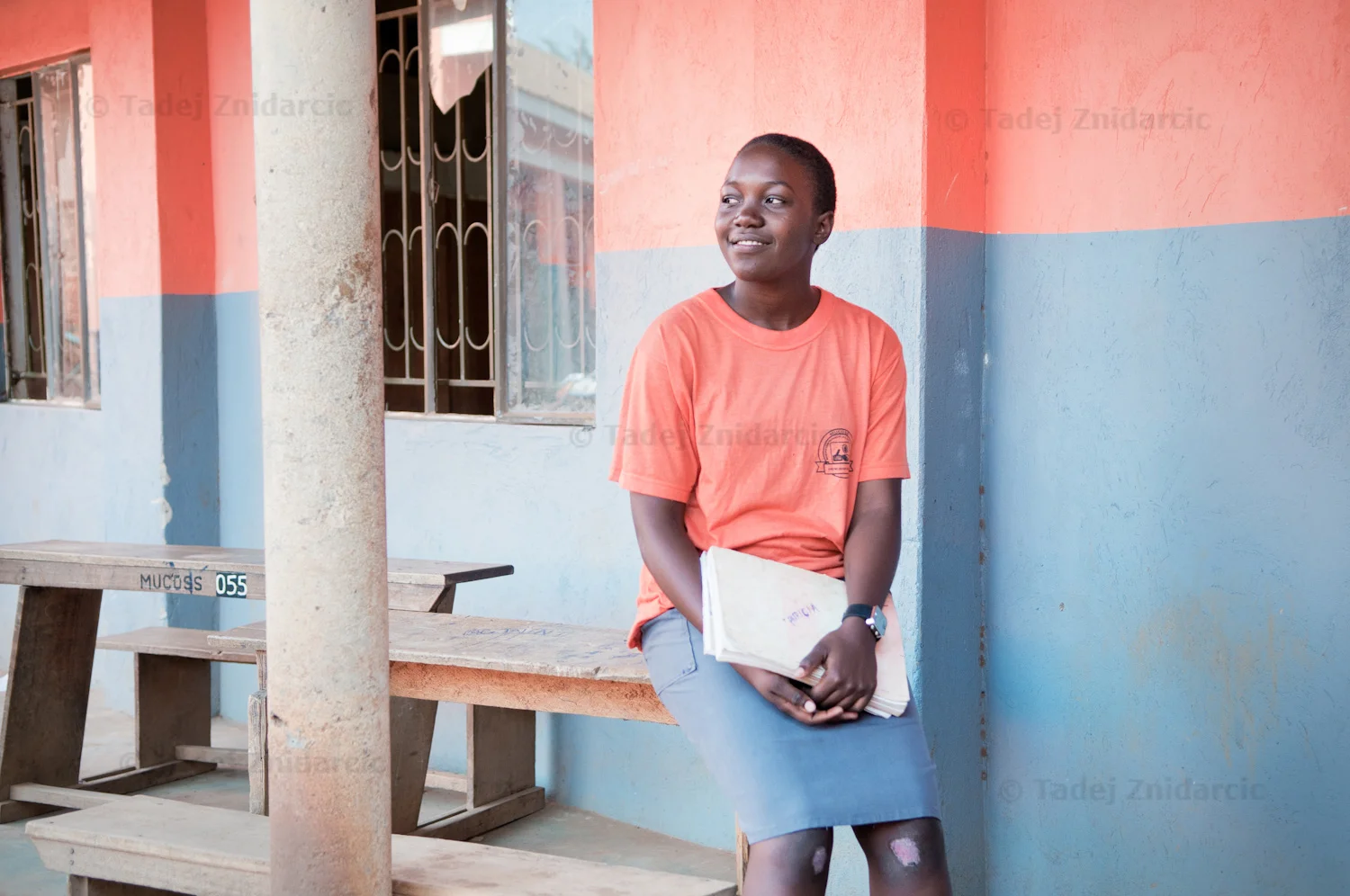 Namuwaya Patricia sits on a bench outside of a classroom at her secondary school, Mukono Comprehensive Senior School in Bweyogerere, Kampala, Uganda. On her knees she has wounds from falling during inline skating practice.