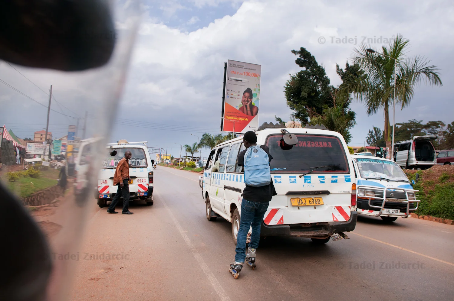 Skater holds on to the back of a commuter minivan on Jinja road in Kampala, Uganda. Some skaters do this to travel faster, but Uganda Skating Federation discourages the practice. There have been reports of injuries and even deaths among youth that hold on to vans.