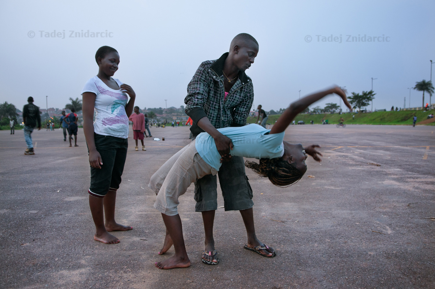At the end of the skating practice at Mandela National Stadium's parking lot in Kampala, Uganda, Kisitu Joseph helps Birungi Janat make a back handstand while Namuwaya Patricia watches.