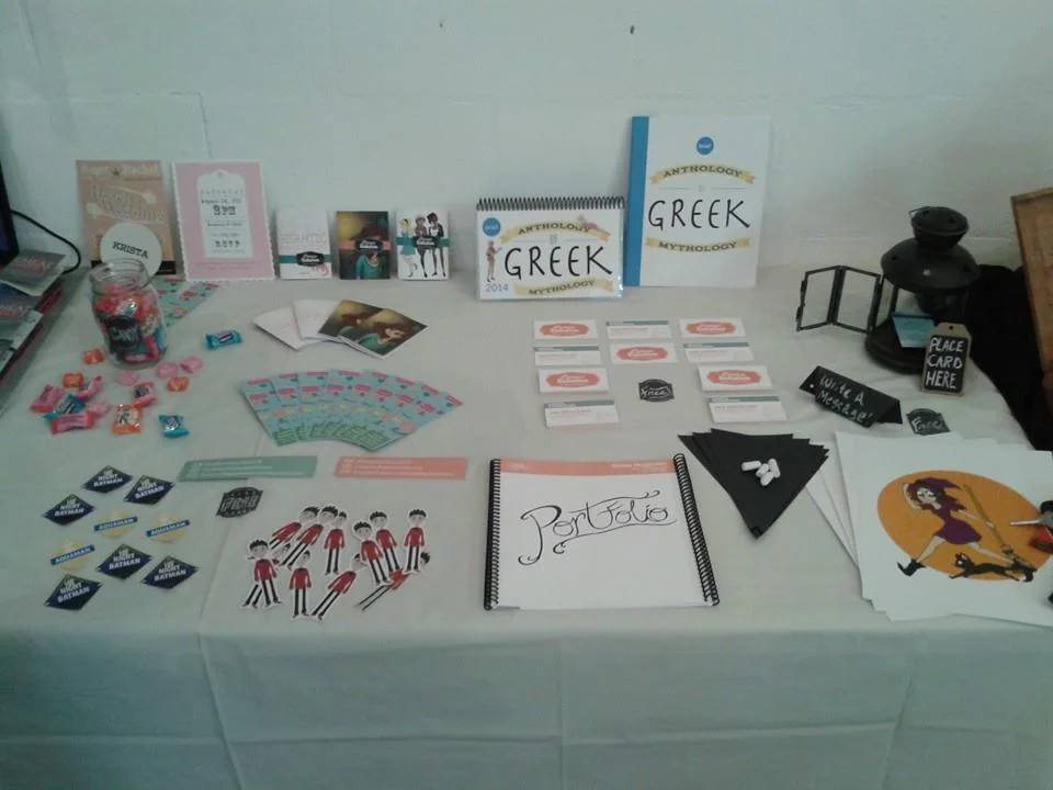 My display table with various Self Promotional items including: Business Cards, Prints, Stickers, Sketchbooks and Contact Bookmarks