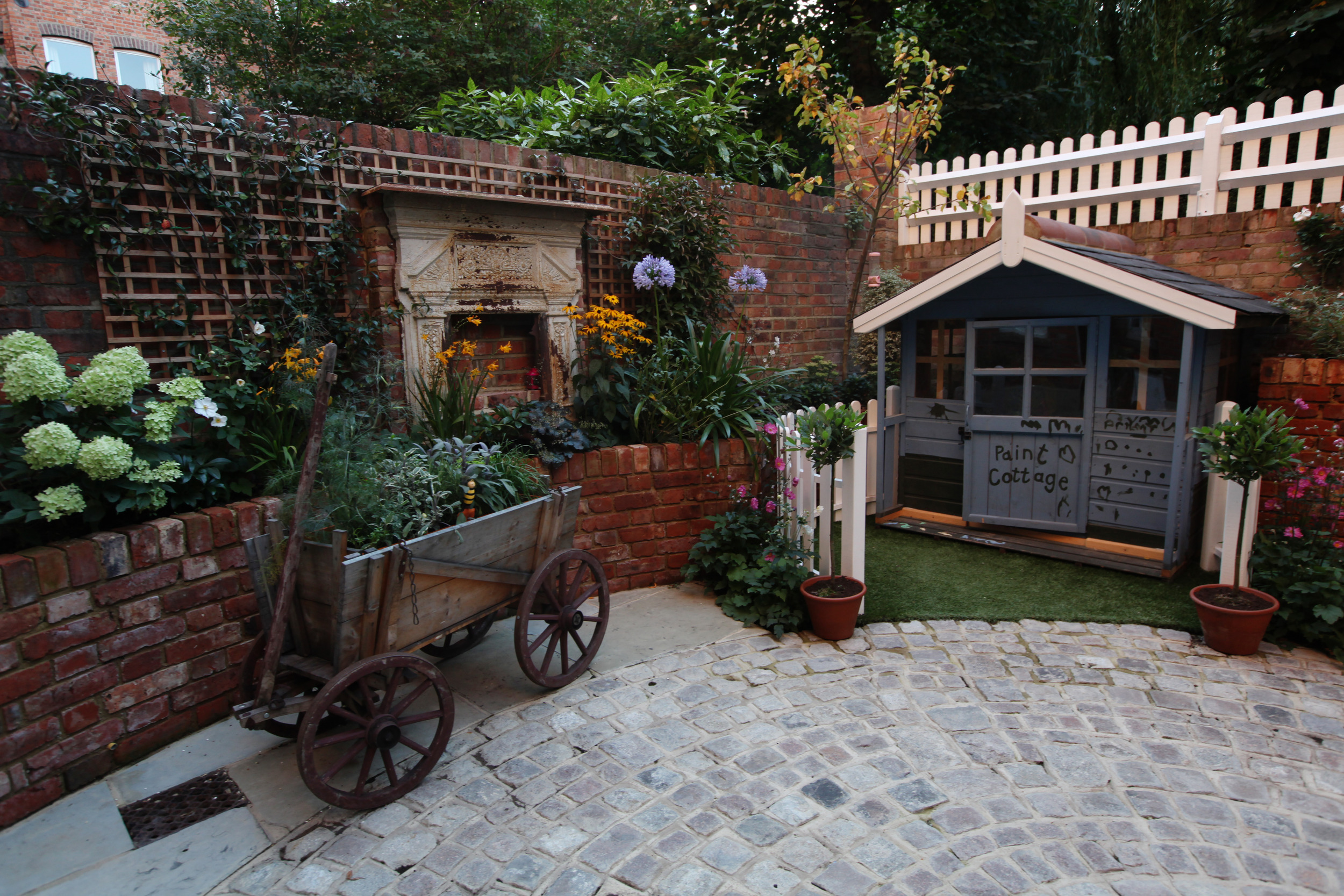 Fun garden design idea with play house, hand cart and fireplace