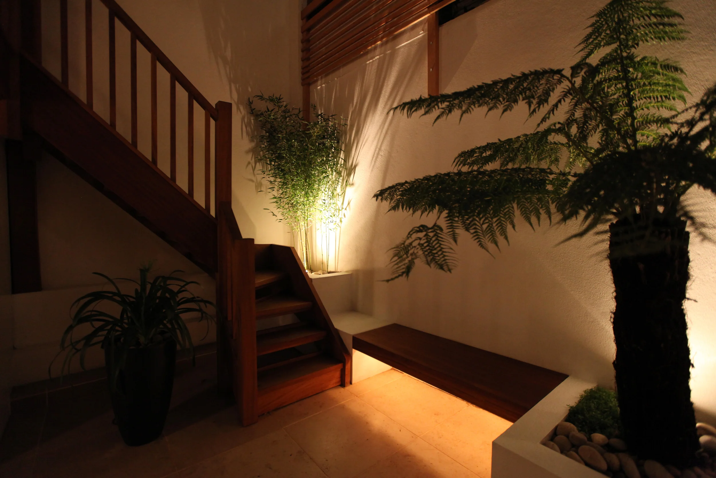  Small shady London town garden at night with lighting and a wooden staircase. 