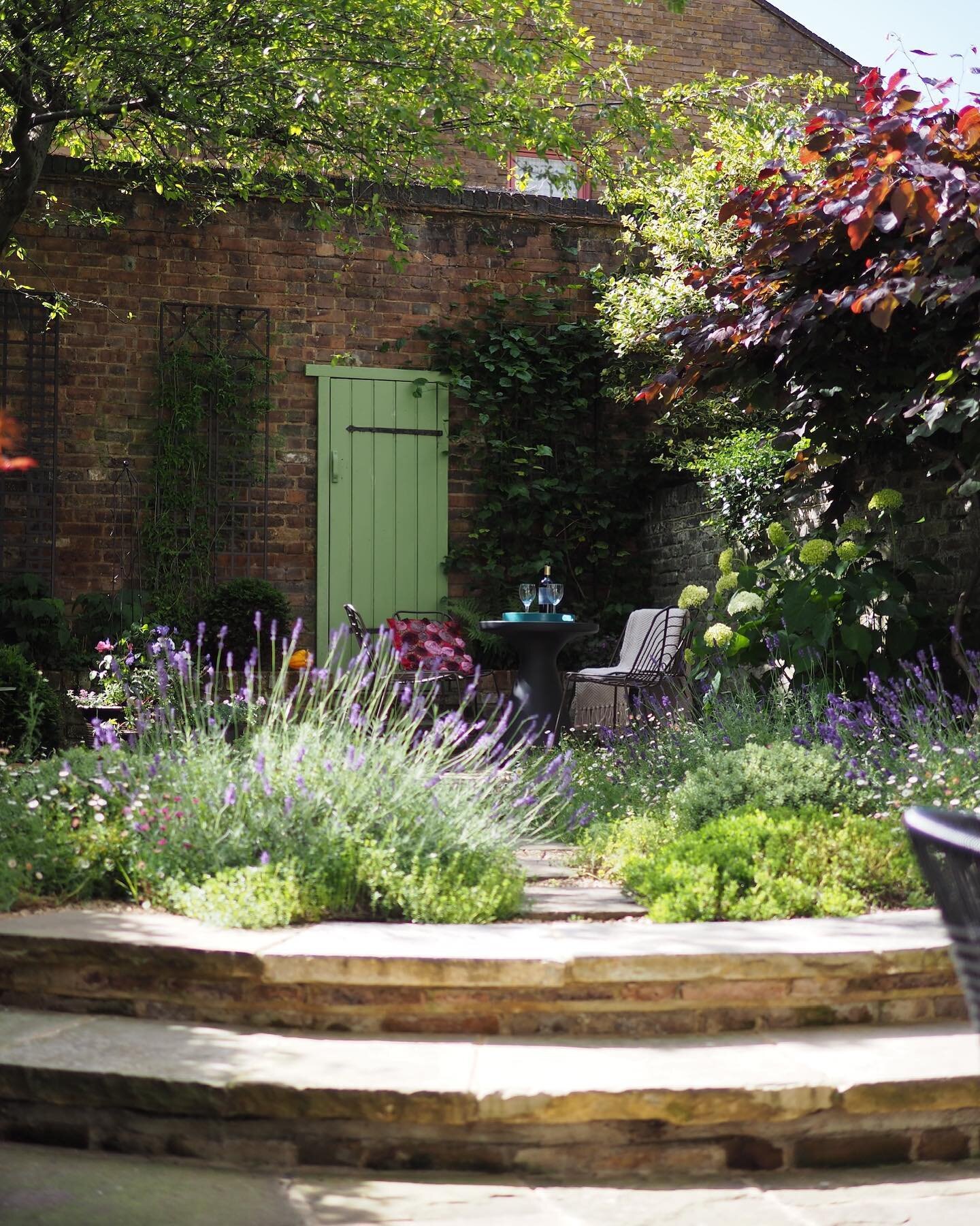 Steppingstones through low mounds of mediterranean planting create a beautiful journey in this north London small courtyard garden. The false door in the rear wall gives a sense of space beyond, opening this beautiful enclosure out in the mind&rsquo;