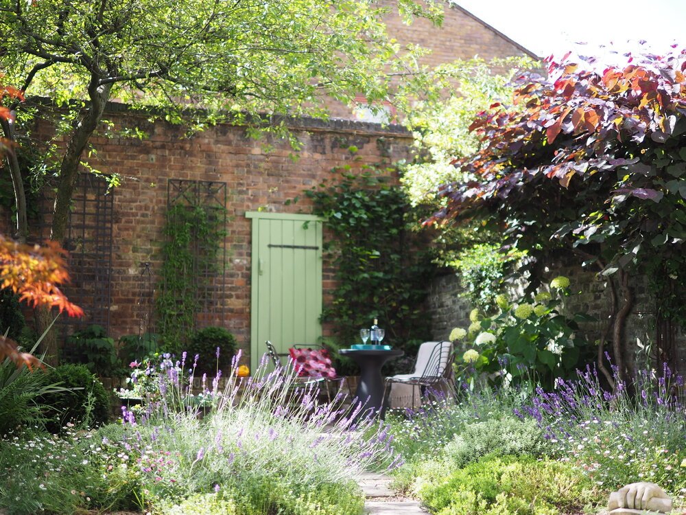  Stunning North London traditional courtyard garden design with yorkstone stepping stones leading through the lavender to a sunny patio witha false door in the brick wall. 