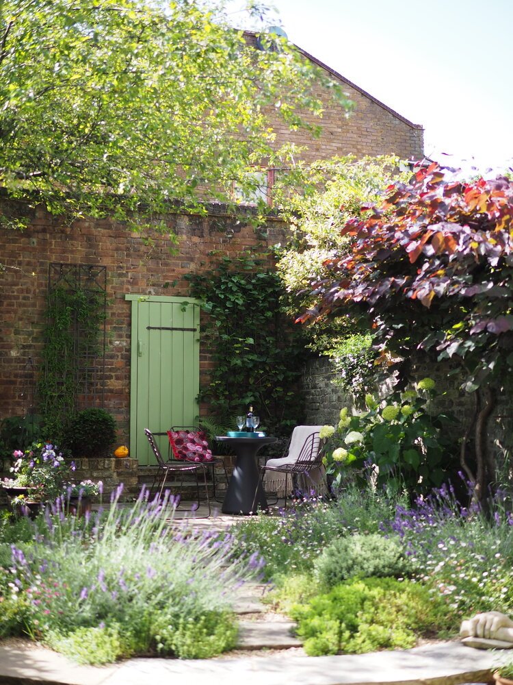  Courtyard garden designed by Living Gardens in London with reclaimed materials, perennial flower beds and a patio with table and chairs. 