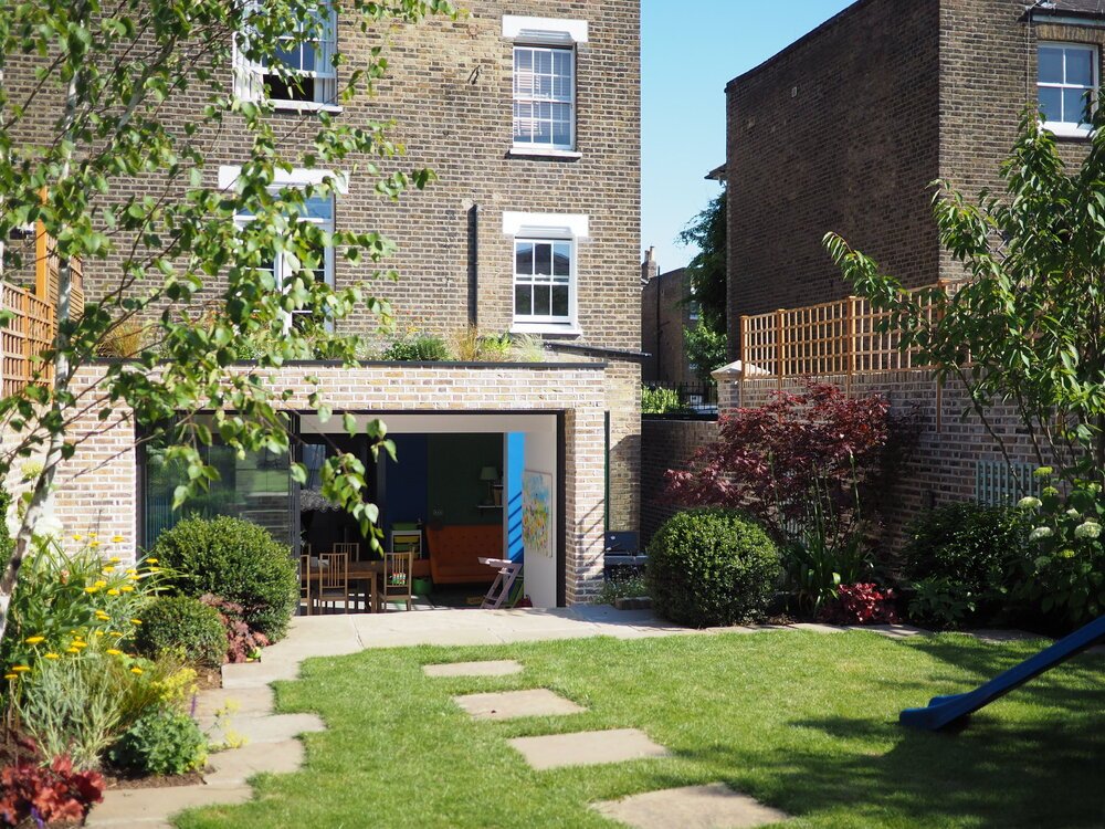  Family friendly garden design in North London with stepping stones, flower borders ad steps leading down to the new extension 