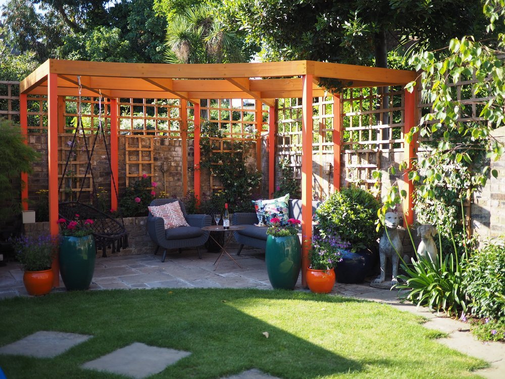  An orange pergola sits in the corner of a beautifully redesigned North London family garden with a seating area on the patio. 