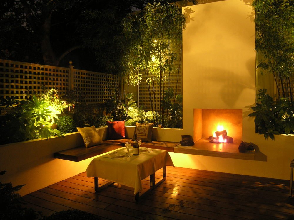  Modern North London town garden at night with a fire in the outdoor chimmney and an elegant table on the hardwood decking. 