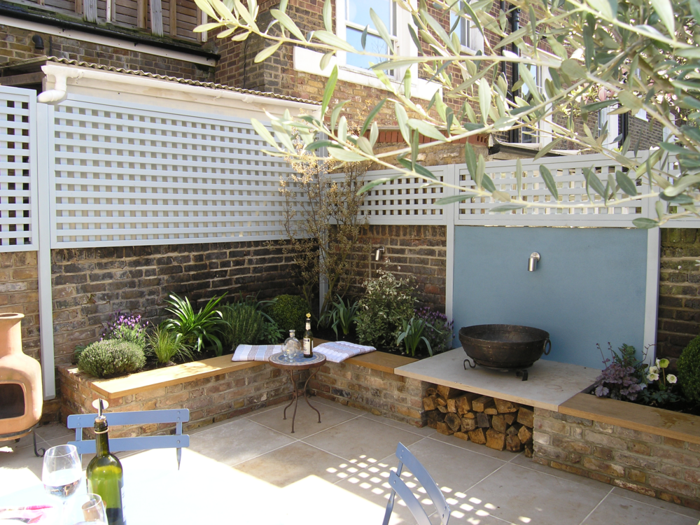  Sunny North London courtyard garden with a large patio for dining, an outdoor fire bowl on a limestone plinth and planting  in keeping with the Provencal theme.  