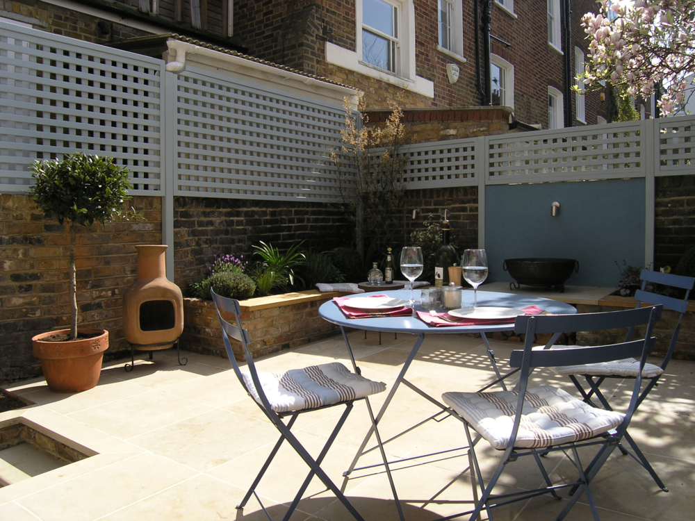  Small garden in North Islington redesigned by Living Gardens with a large limestone patio for dining, reclaimed brick planters and bay trees in teracotta pots. 