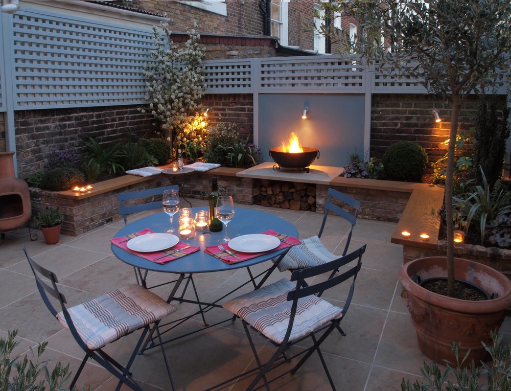  Islington courtyard garden with large patio for dining surrounded by planters made of reclaimed bricks that provide more seating for socialising around the open fire. 