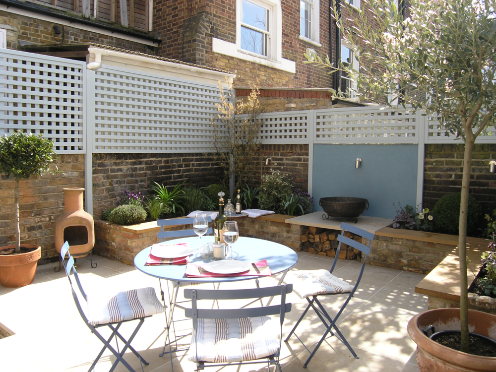  Small courtyard garden design in London with limestone patio for dining, fire bowl and seating around the raised planters. 