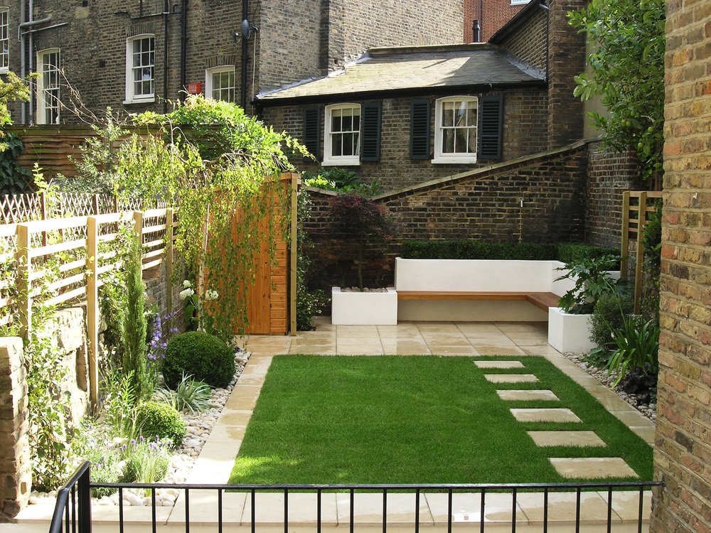  Contemporary garden design in N1 with light limestone paving surrounding the lawn leading to a patio with modern floating, L-shaped Iroko bench. 