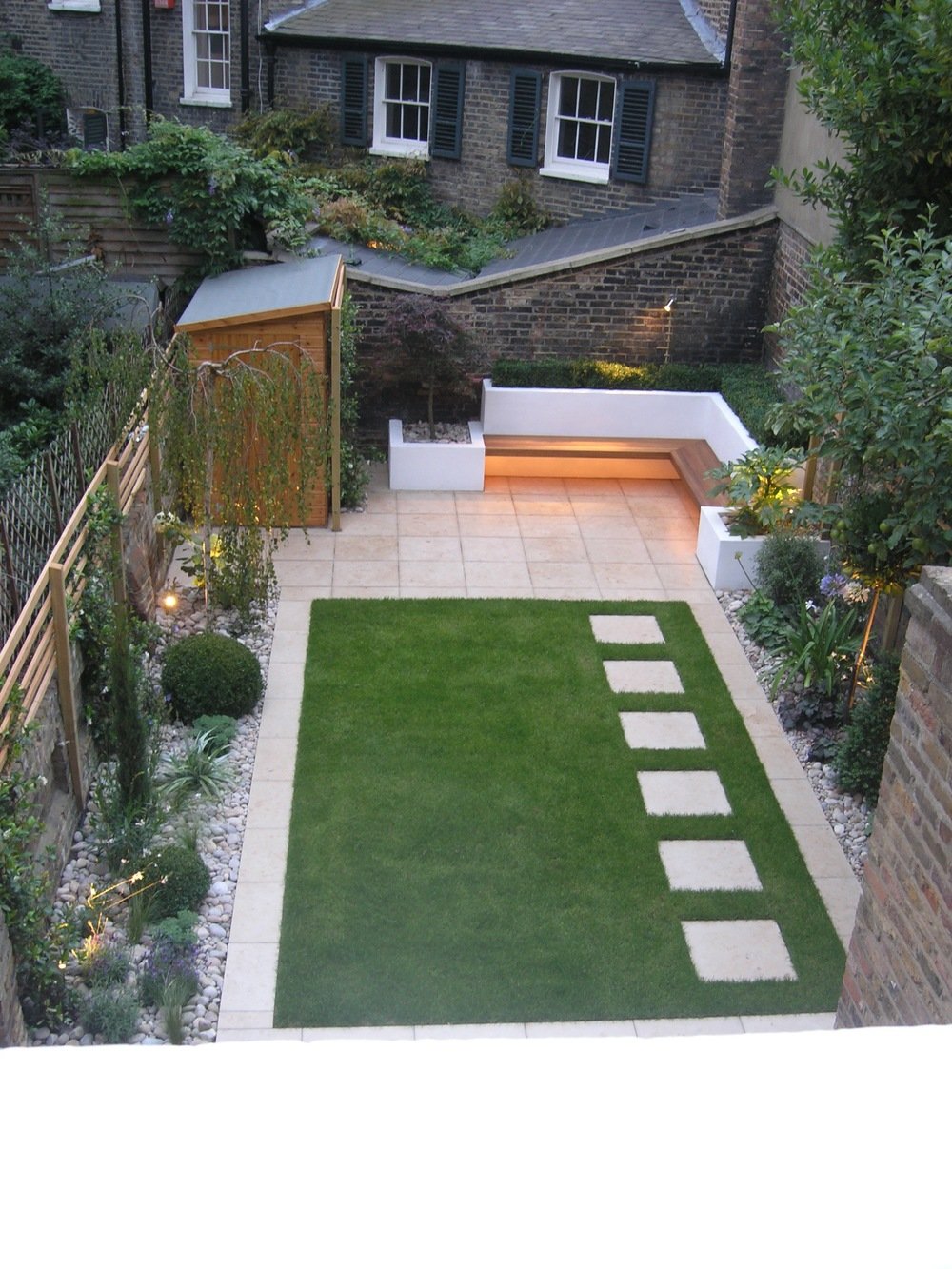  Bespoke garden design in North London for a period property with limestone paving surrounding a lawn and stepping stones leading to a modern seating area. 