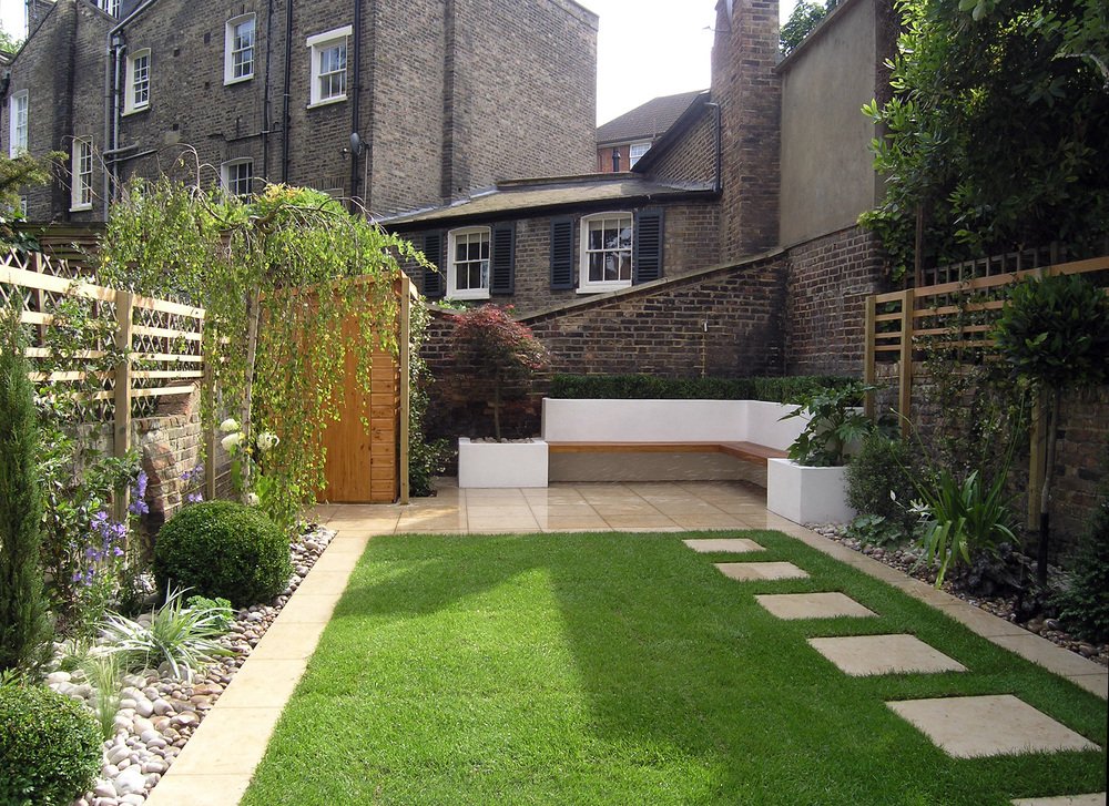  Low maintenance garden design in North London with selected structural herbaceous perennials flanking a rectangular lawn that leads to a bespoke seating area with a floating bench. 