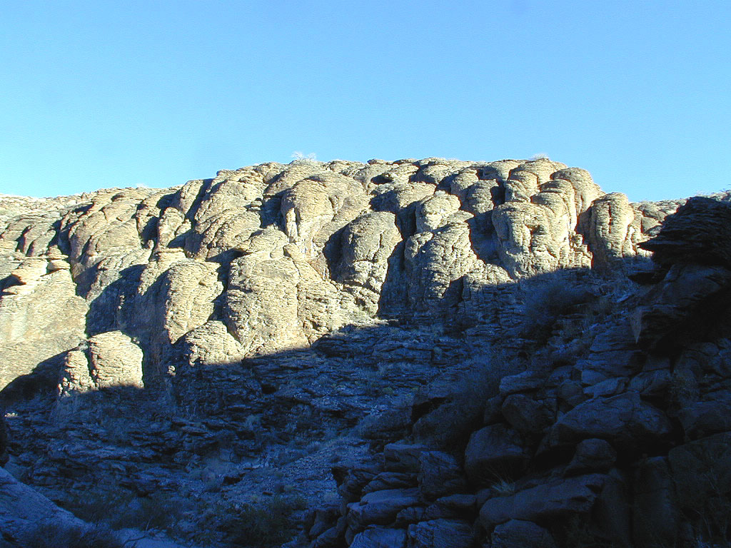 Shadows creep into the wash. Sedimentary layered rock stands out well in this light.