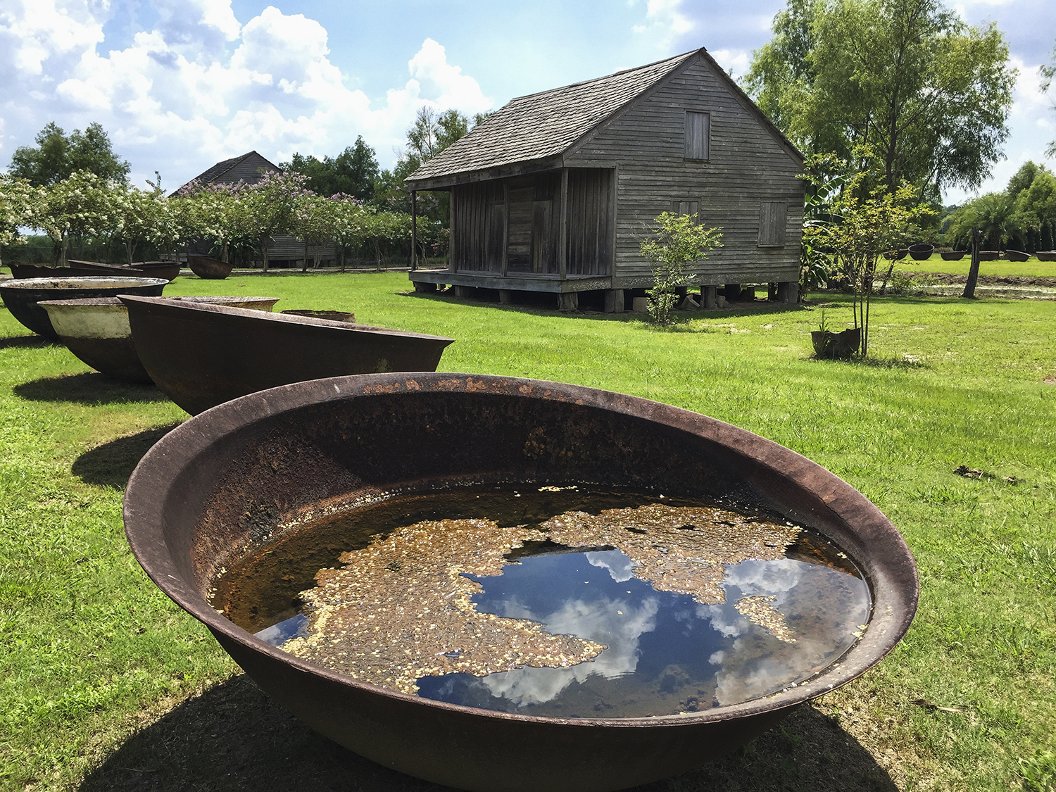 A cabin once inhabited by enslaved people (on a different plantation), with sugar kettles in the foreground. Whitney Plantation, Wallace, Louisiana, July 2015. Photo: EHP