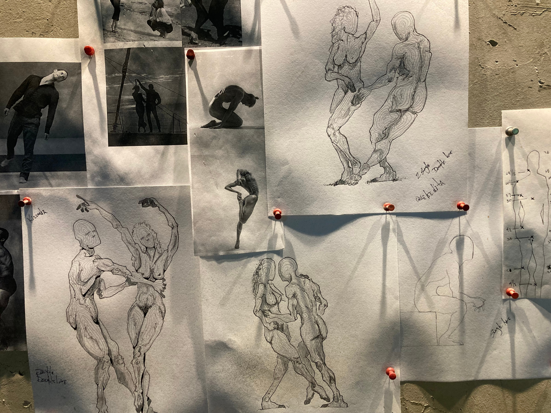 Early sketches and research photos pinned to a wall and cast in shadow of artist J. Aaron Alderman's dancing figure sculptures.