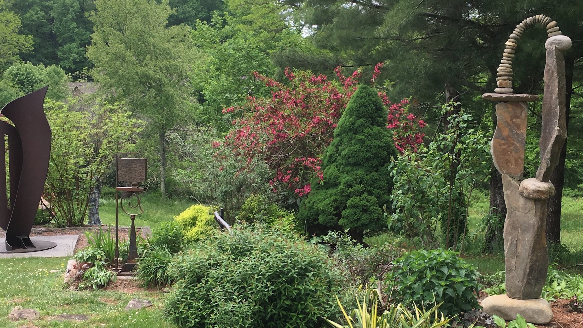 A view of the Anvil Arts sculpture garden in summer. Several large scale outdoor sculptures dot a lovely garden landscape.  