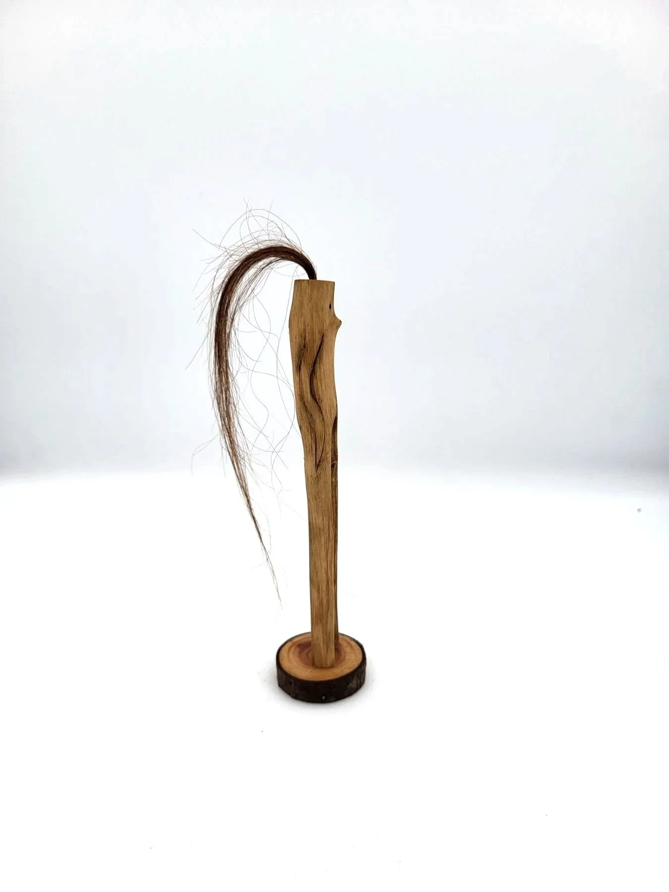 Hand-carved wooden tree creature with long strand of brown hair facing sideways