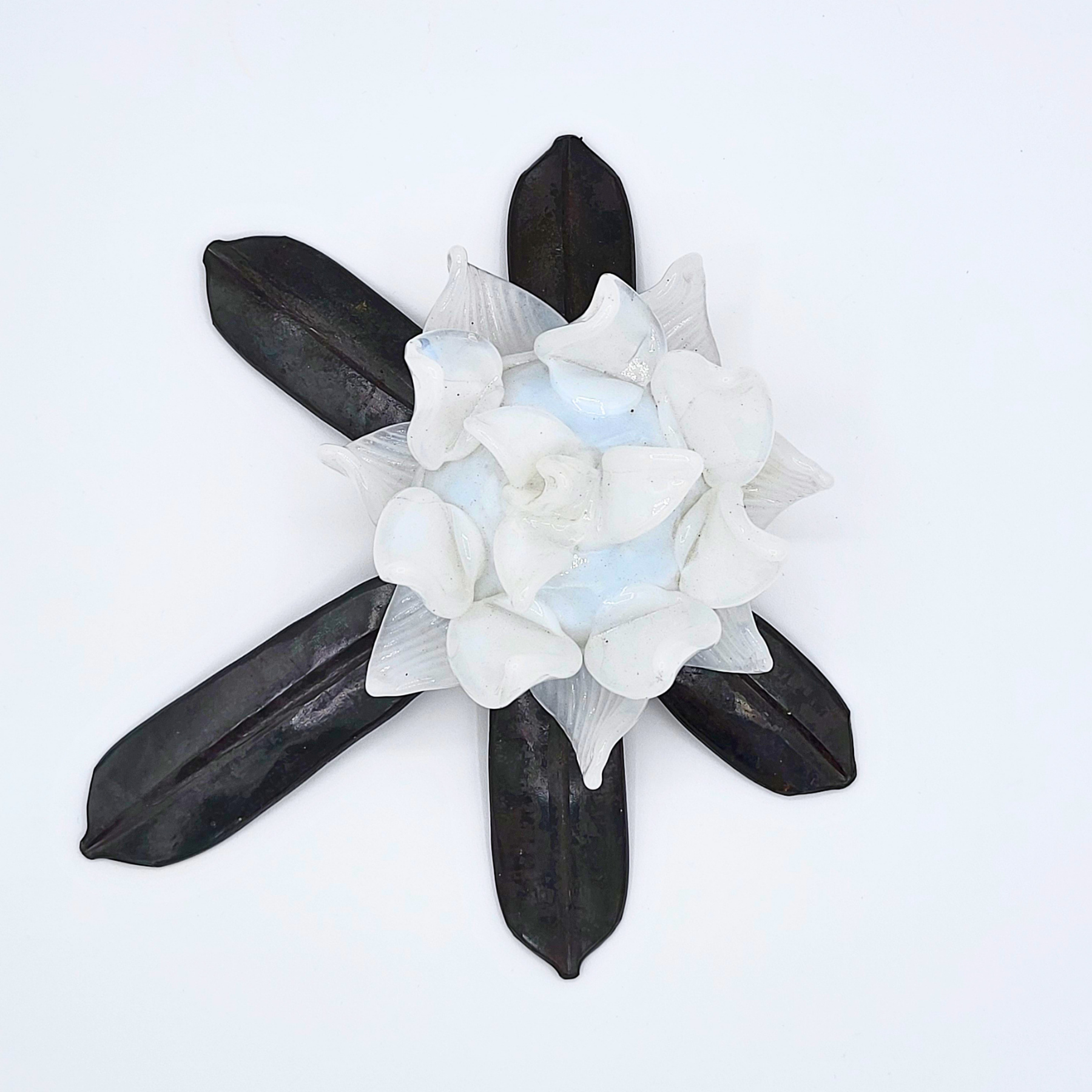 Hand-forged rhododendron leaf with white glass flower nestled in the center against a white background.